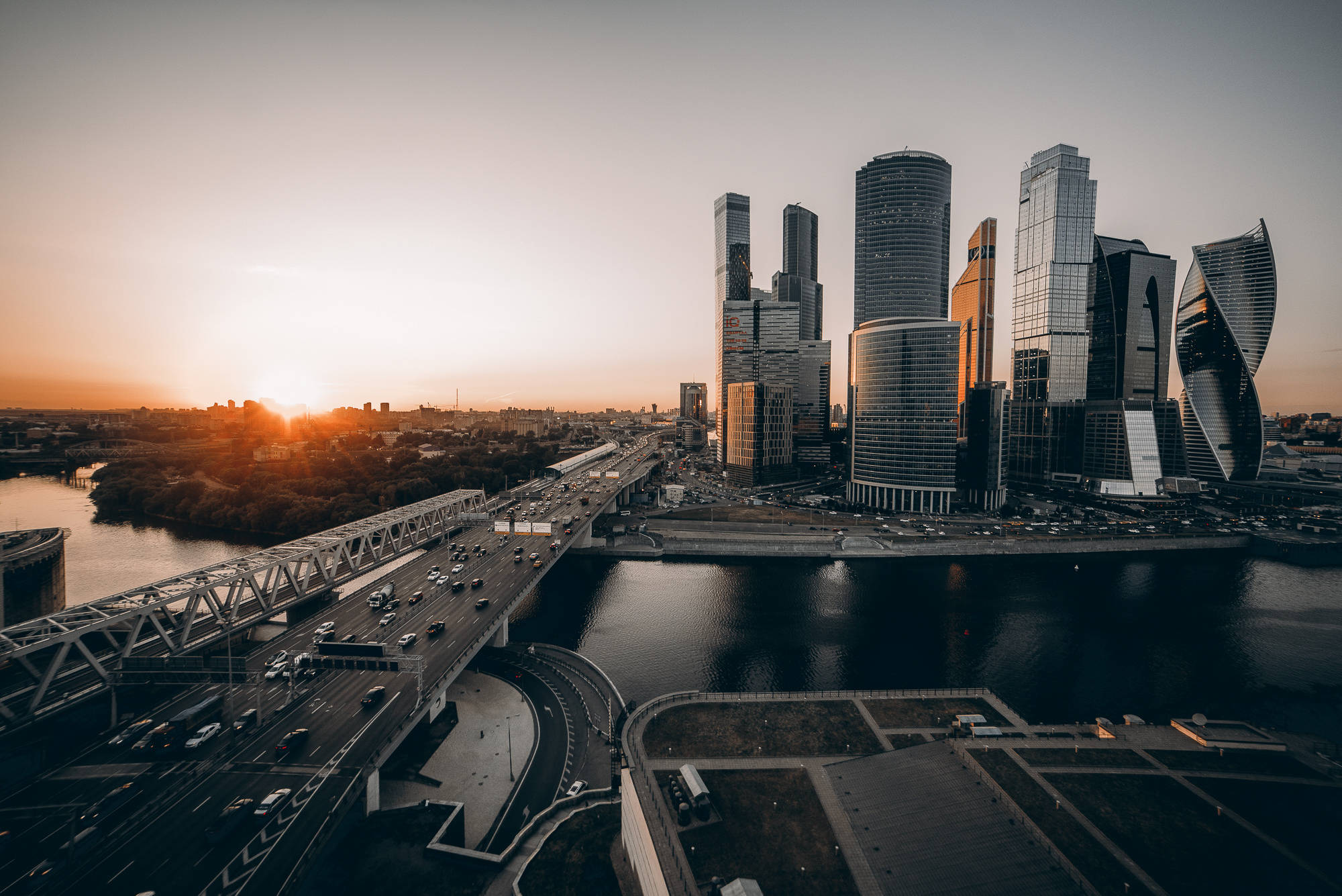 Russia 桌布 壁紙 — 夕陽灑落在現代摩天大樓和一條繁忙的橋樑上，橫跨河流，構成廣闊的城市天際線。