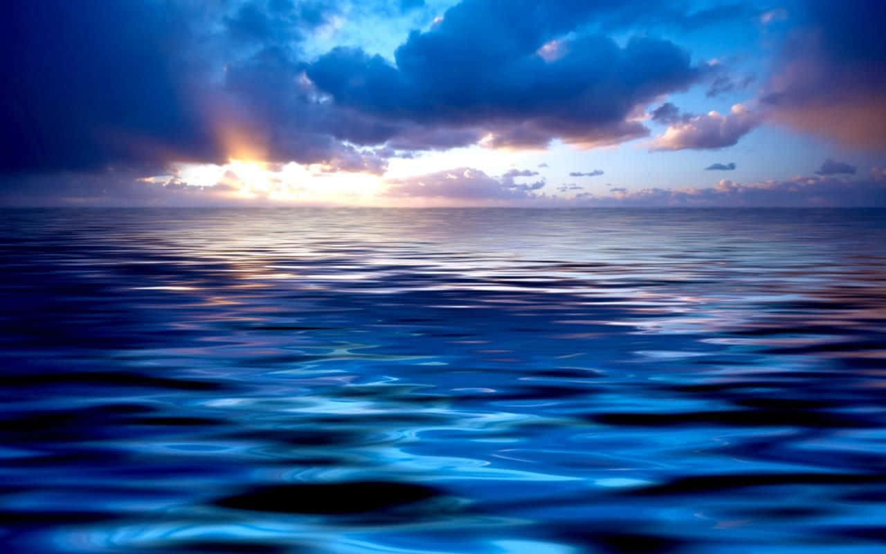Blue Horizon 桌布 壁紙 — 夕陽穿透烏雲，在暮色中將金色光芒灑在廣闊平靜的海洋上。