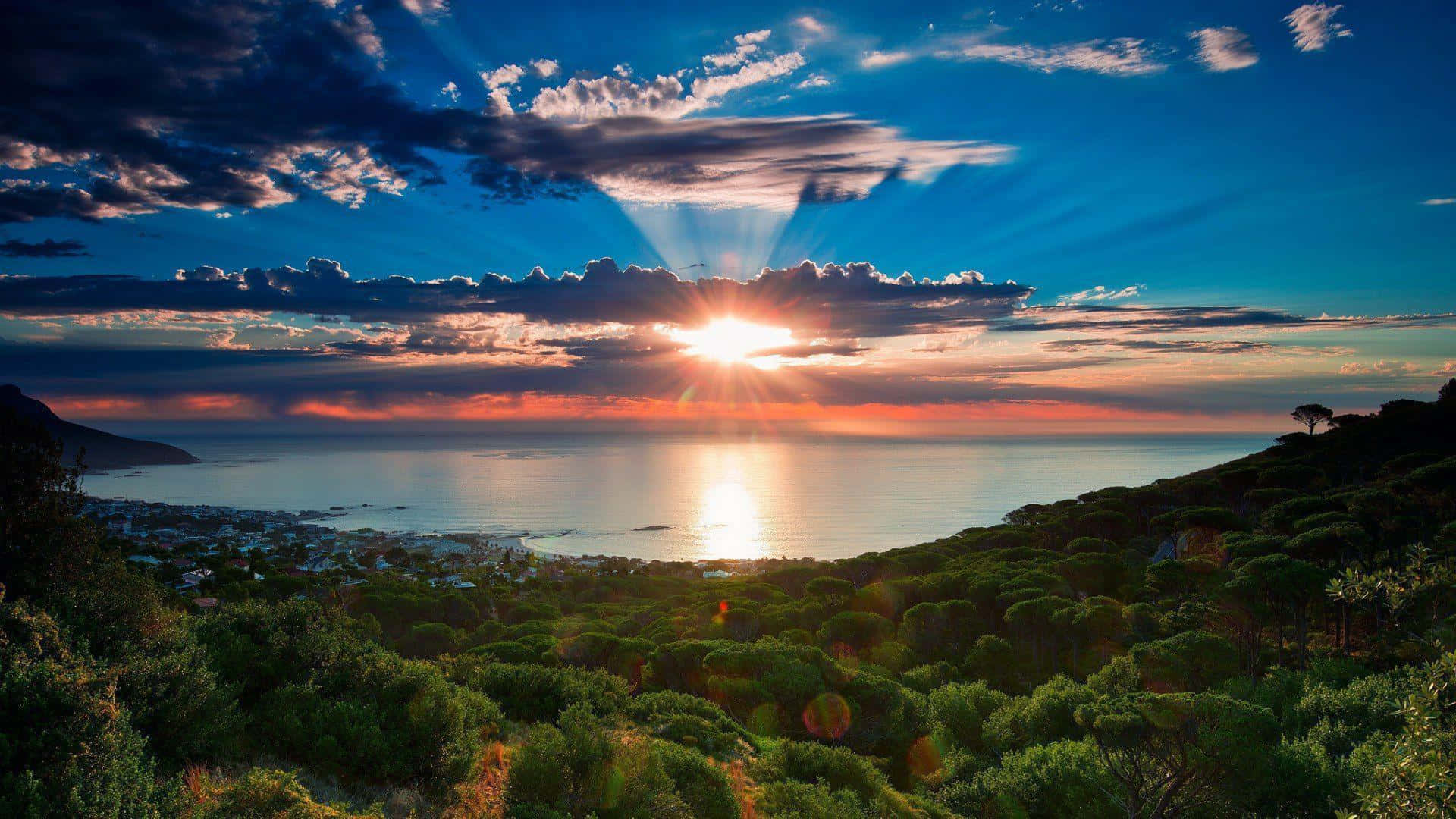 South Africa 桌布 壁紙 — 夕陽穿透雲層，照射在坐落於綠色山丘之間的沿海小鎮上。