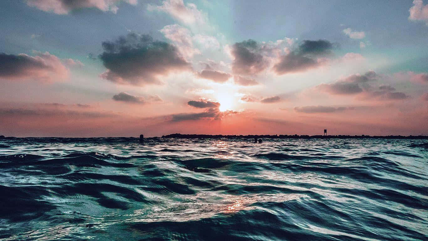 海邊美學 桌布 壁紙 — 夕陽穿過雲層，照耀在波光粼粼的海面上，遠方陸地輪廓隱約可見。