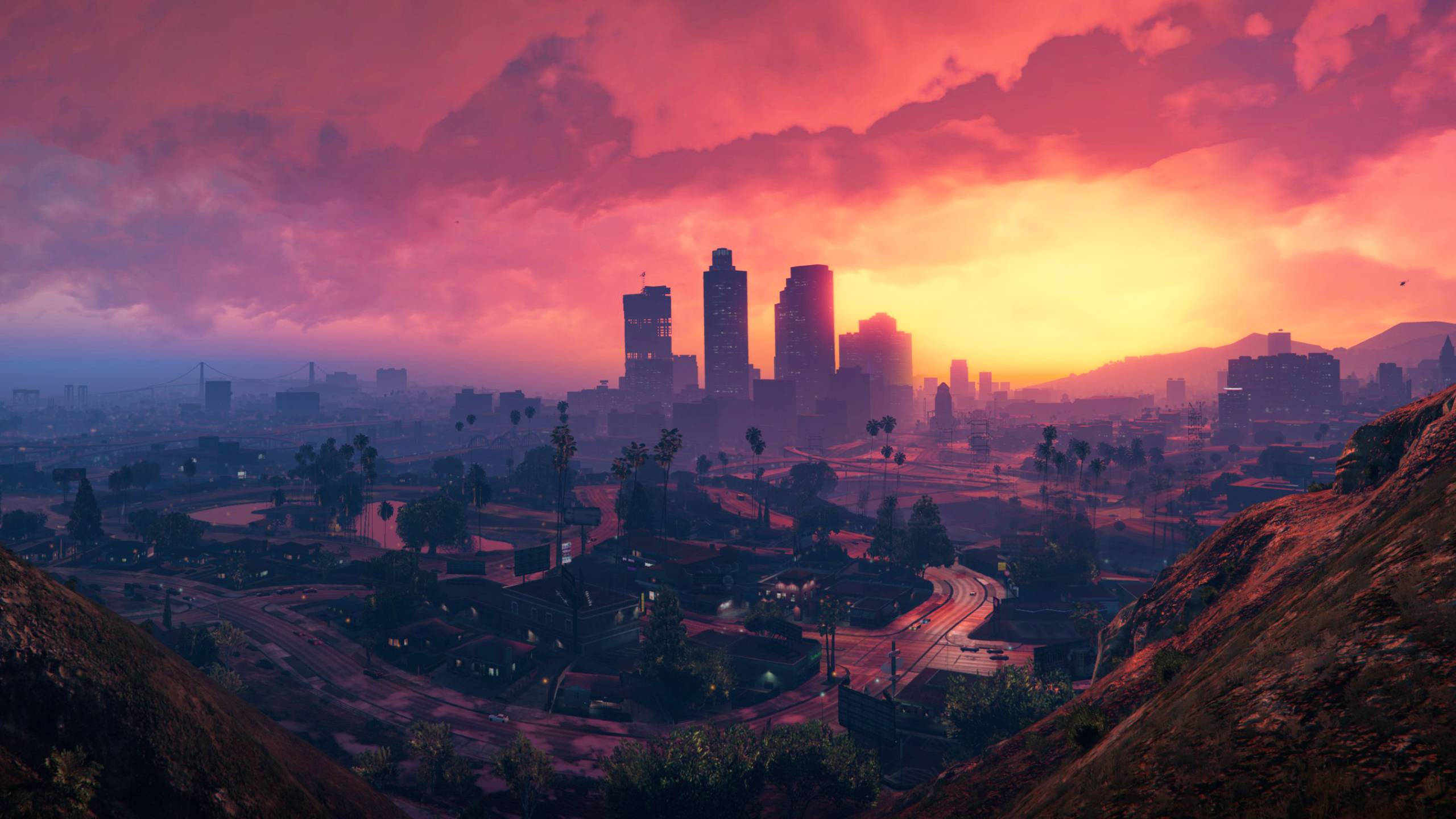 gta v 桌布 壁紙 — 夕陽西下，絢麗的晚霞以火紅的粉紅和橙色色調沐浴著廣闊的城市景觀，摩天大樓在棕櫚樹成蔭的街道上拔地而起。