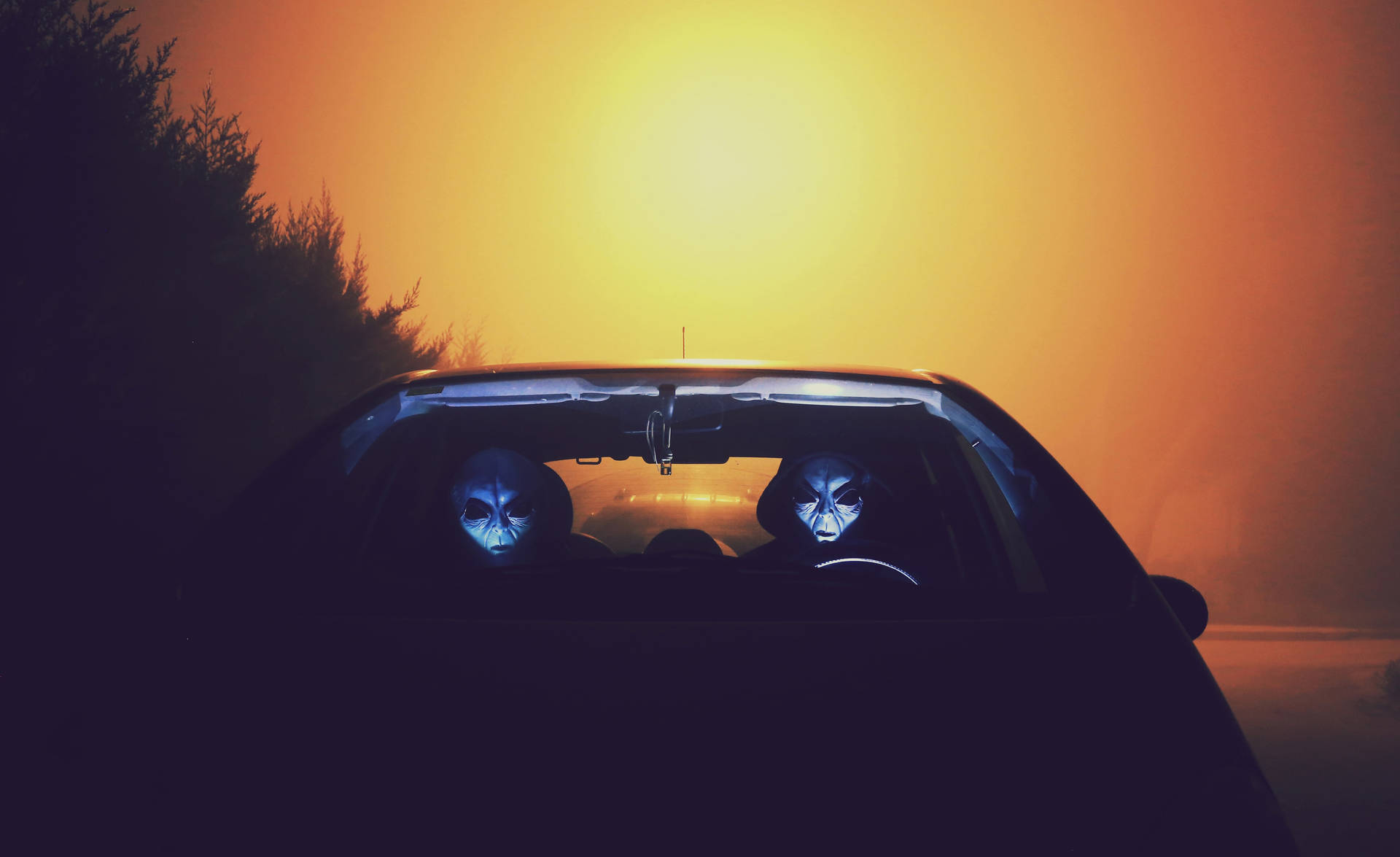 兩個臉部發出藍光的外星人在日落時分駕駛汽車。