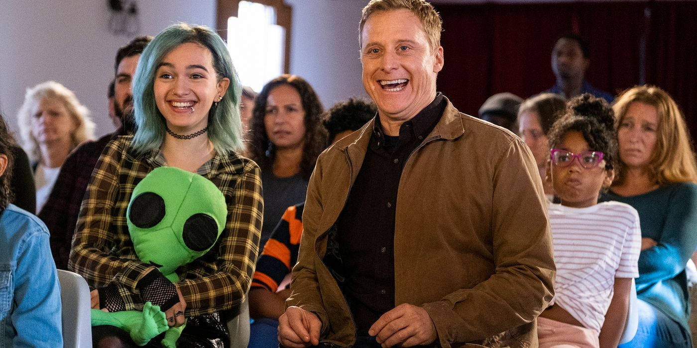 觀眾席上的人們在笑，包括一個拿著綠色外星人毛絨玩具的藍髮女孩。
