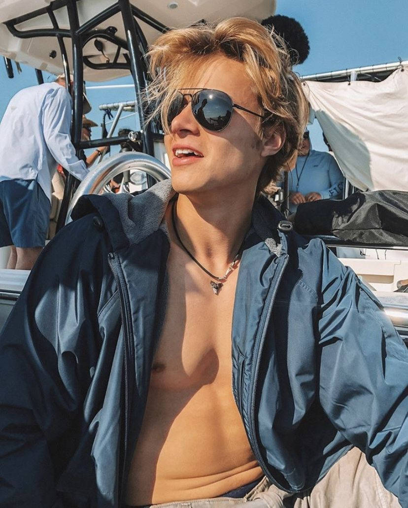 年輕男子戴著太陽眼鏡和敞開的夾克，在陽光明媚的船上。