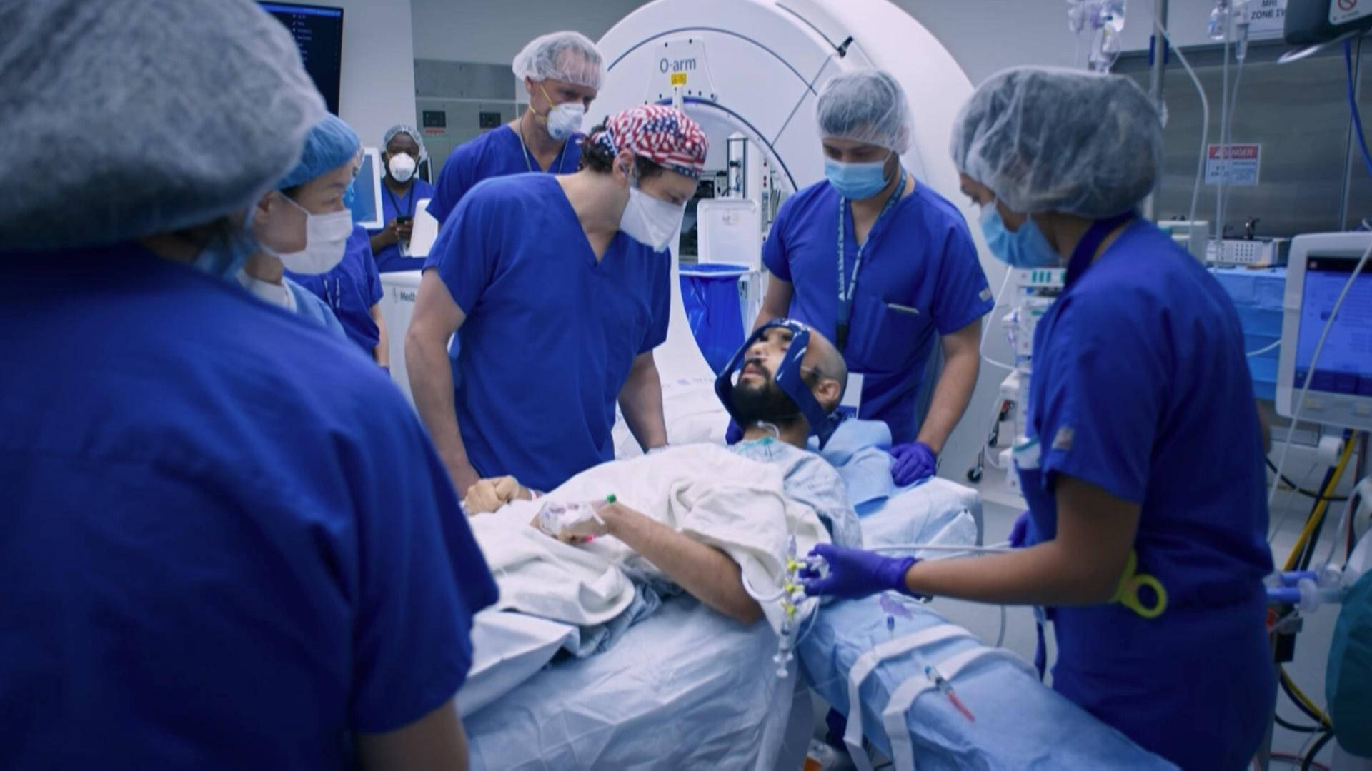 穿著手術服和口罩的醫護人員在MRI機器附近的病床上照顧病人。
