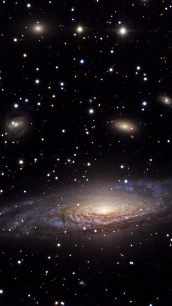 多個星系手機背景 壁紙 — 一個令人嘆為觀止的螺旋星系，在深邃的太空中散發著金色和藍色的光芒，被無數遙遠的恆星所環繞。