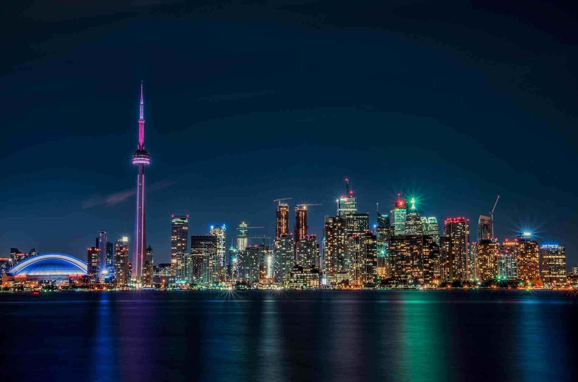 Toronto 桌布 壁紙 — 多倫多夜晚天際線，CN塔發出紫色光芒，城市燈光倒映在平靜的水面上。