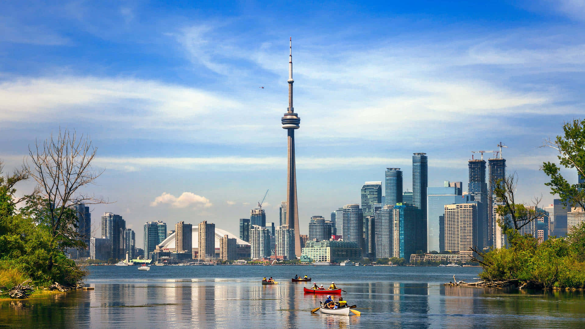 Canada 桌布 壁紙 — 多倫多天際線與CN塔聳立在平靜的湖面上，划艇者在明亮的藍天白雲下划槳。