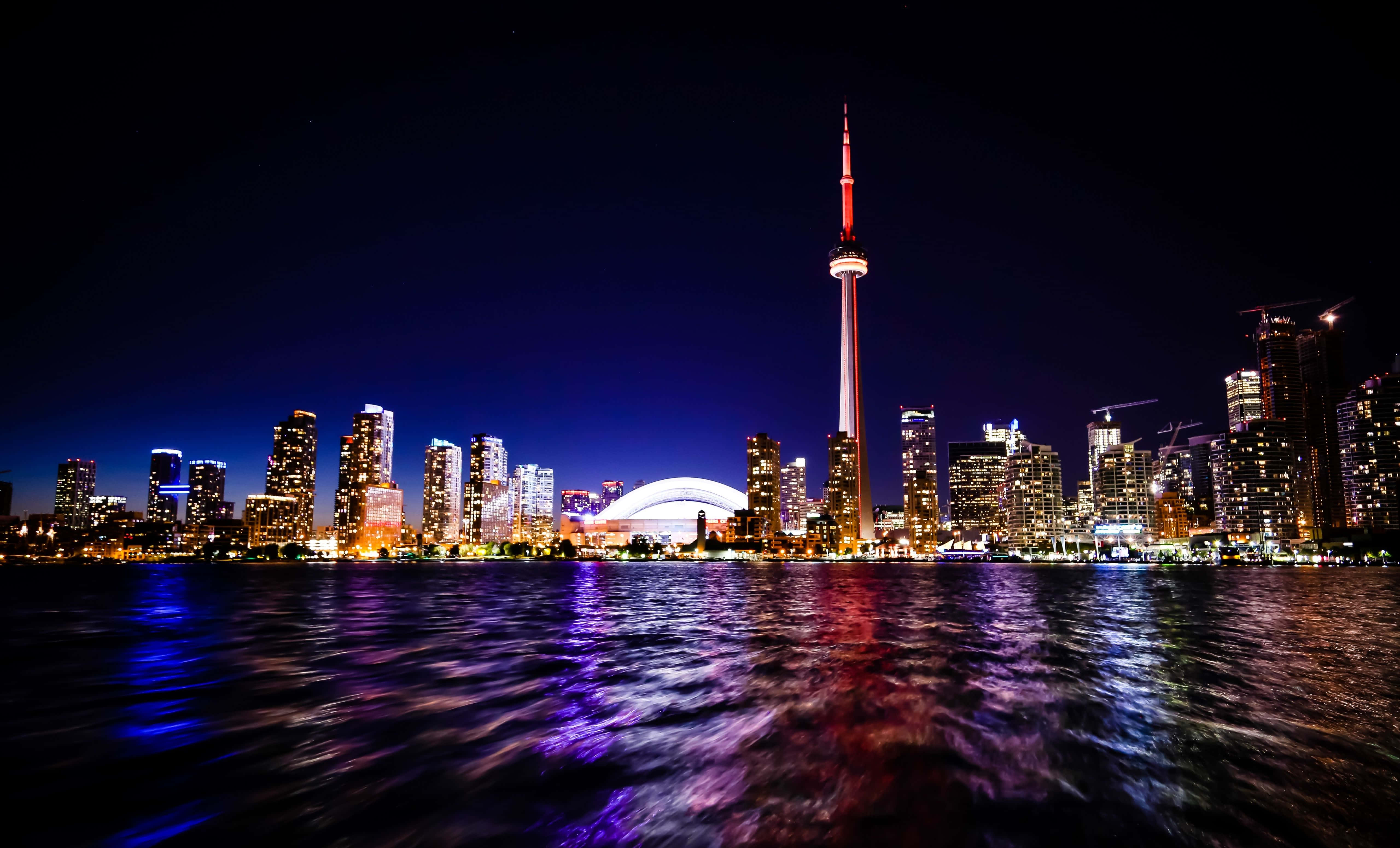 Toronto 桌布 壁紙 — 多倫多的天際線在夜晚閃耀，CN塔以紅藍燈光點亮，倒映在下方黑暗的水面上。