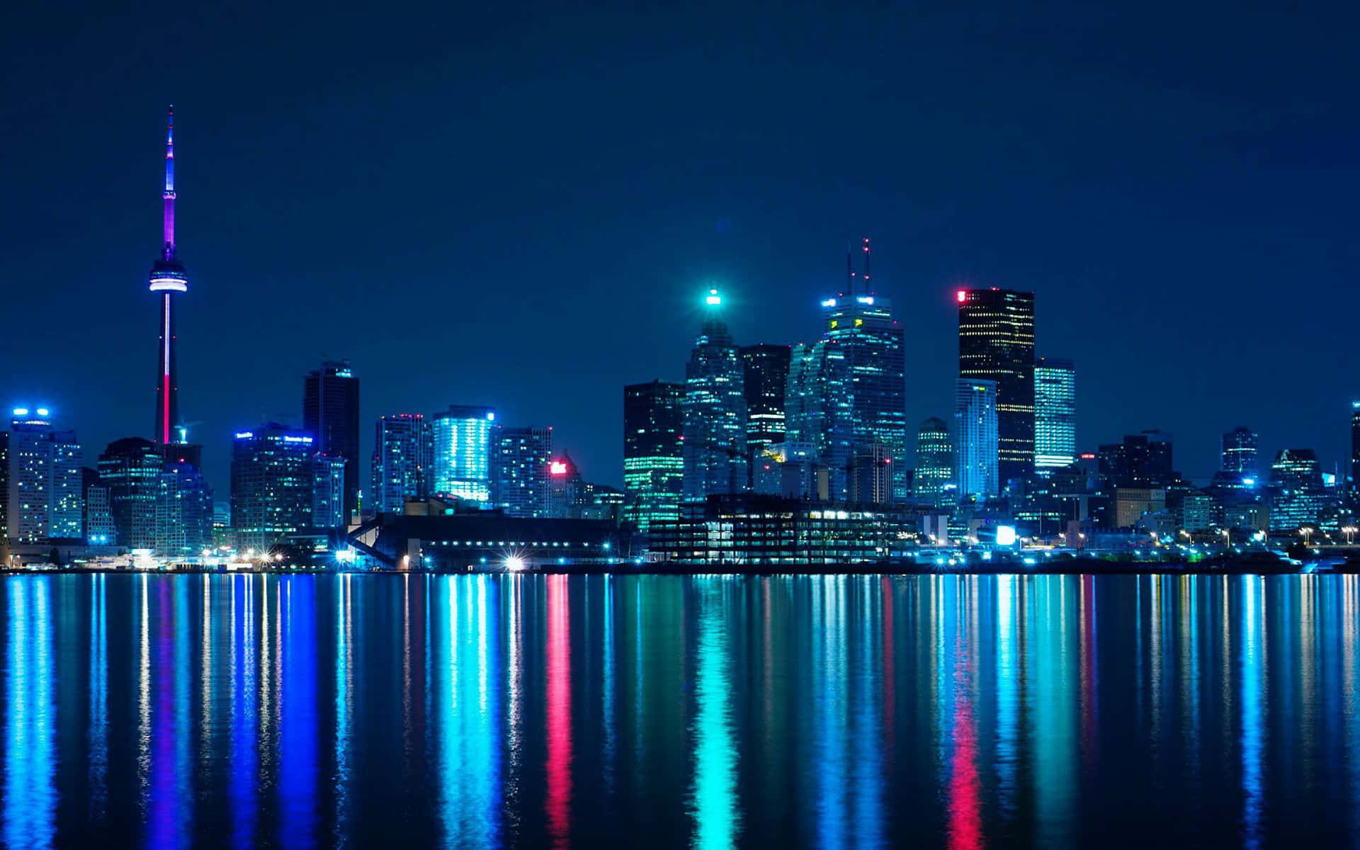 多倫多繁華天際線的空中視角 壁紙 — 充滿活力的夜景城市景觀，有燈火通明的摩天大樓和發光的CN塔倒映在平靜的水面上。