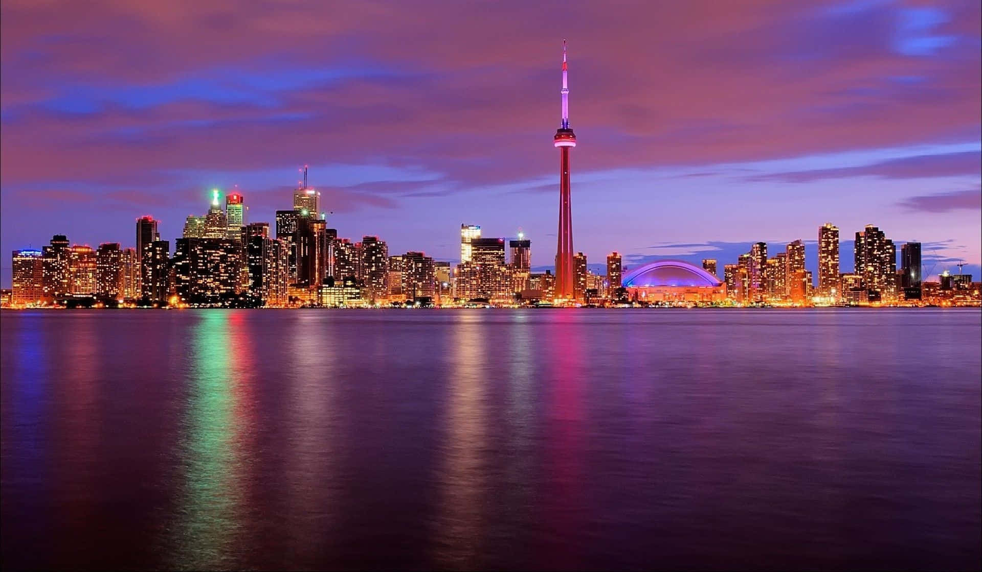 Toronto 桌布 壁紙 — 多倫多黃昏天際線，CN塔在紫色雲彩映襯下發光，倒映在平靜的水面上。