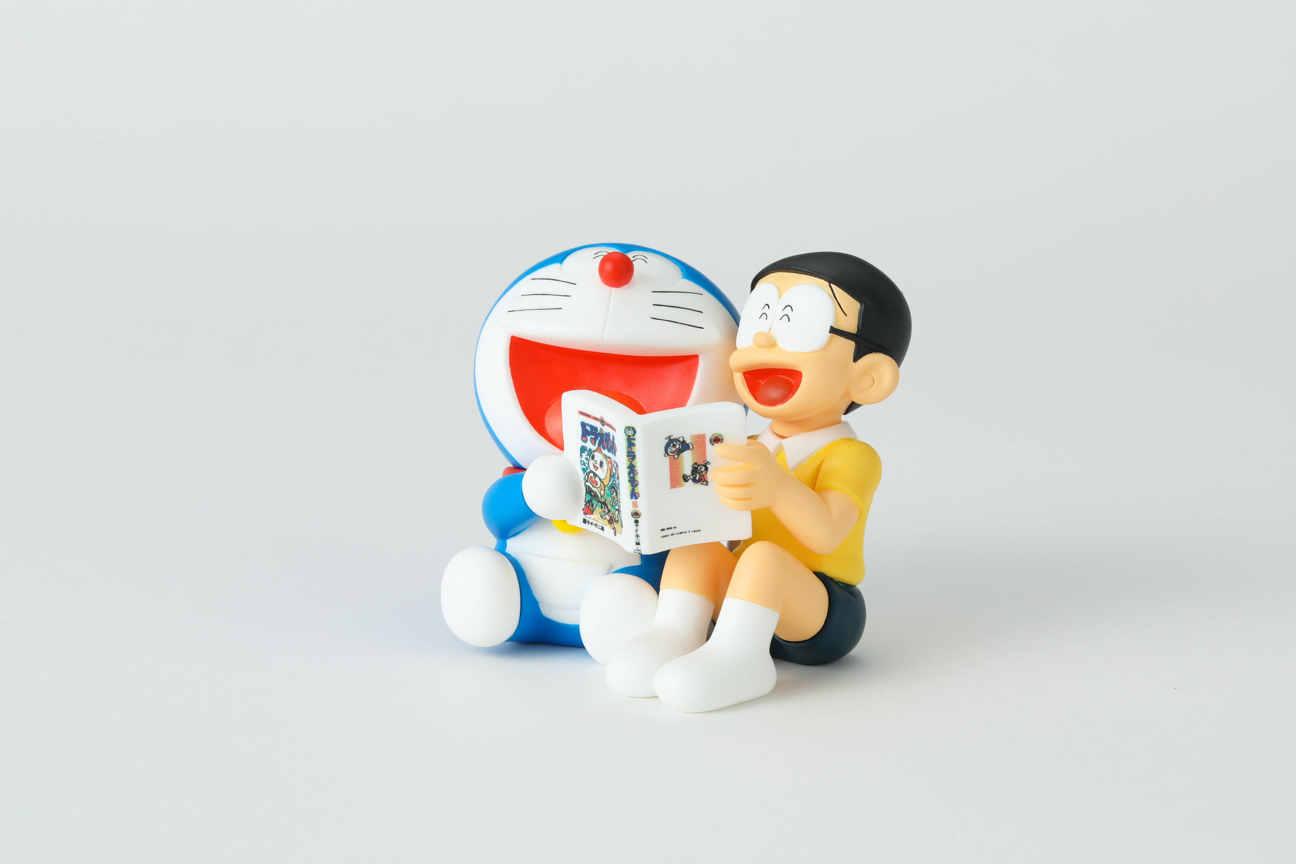 Doraemon 桌布 壁紙 — 多啦A夢和大雄一起坐著，邊看漫畫邊笑，背景是純白色。