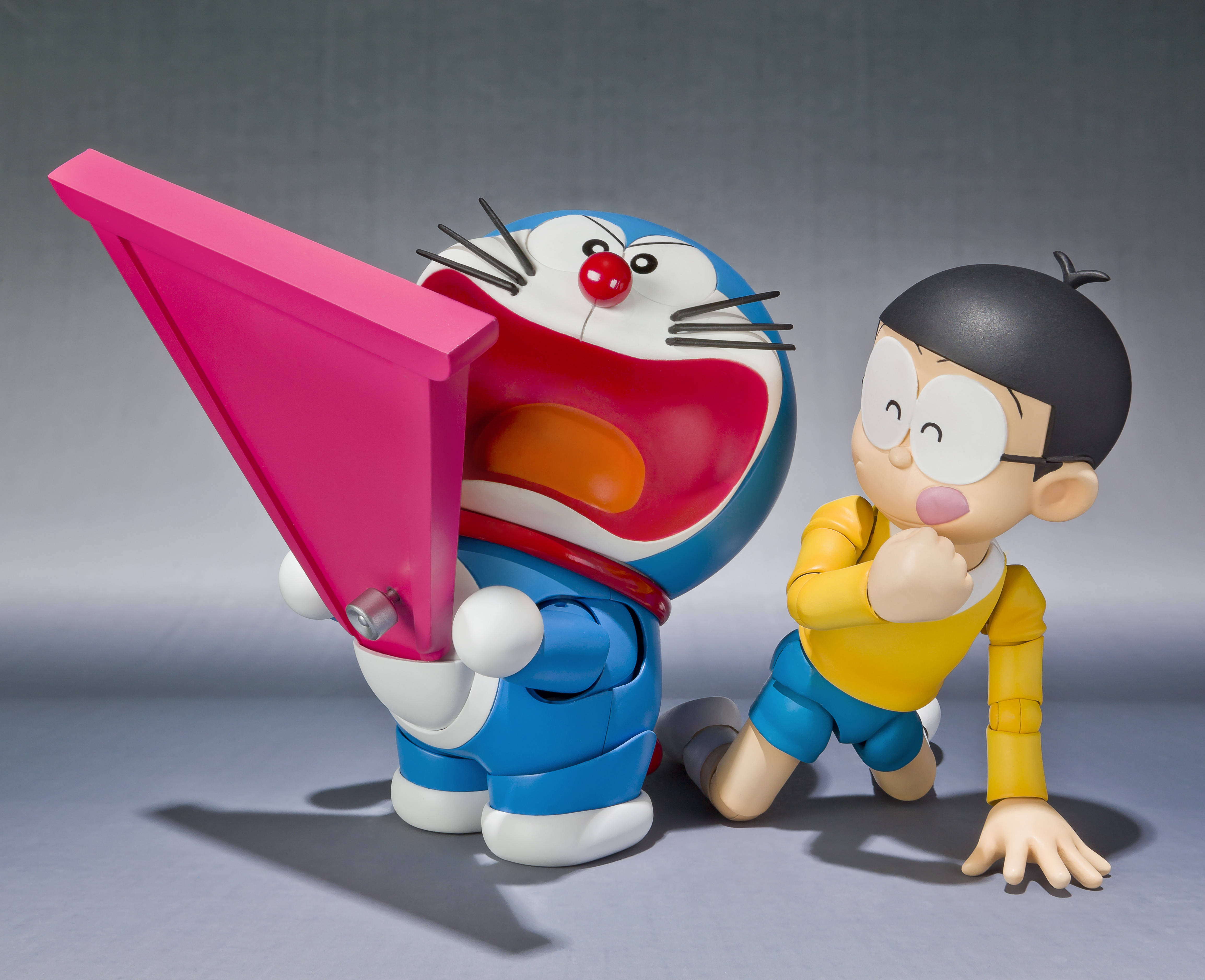 Doraemon 桌布 壁紙 — 多啦A夢和大雄以俏皮的姿勢擺拍，多啦A夢在純灰色工作室背景前拿著一個巨大的粉紅色小工具。
