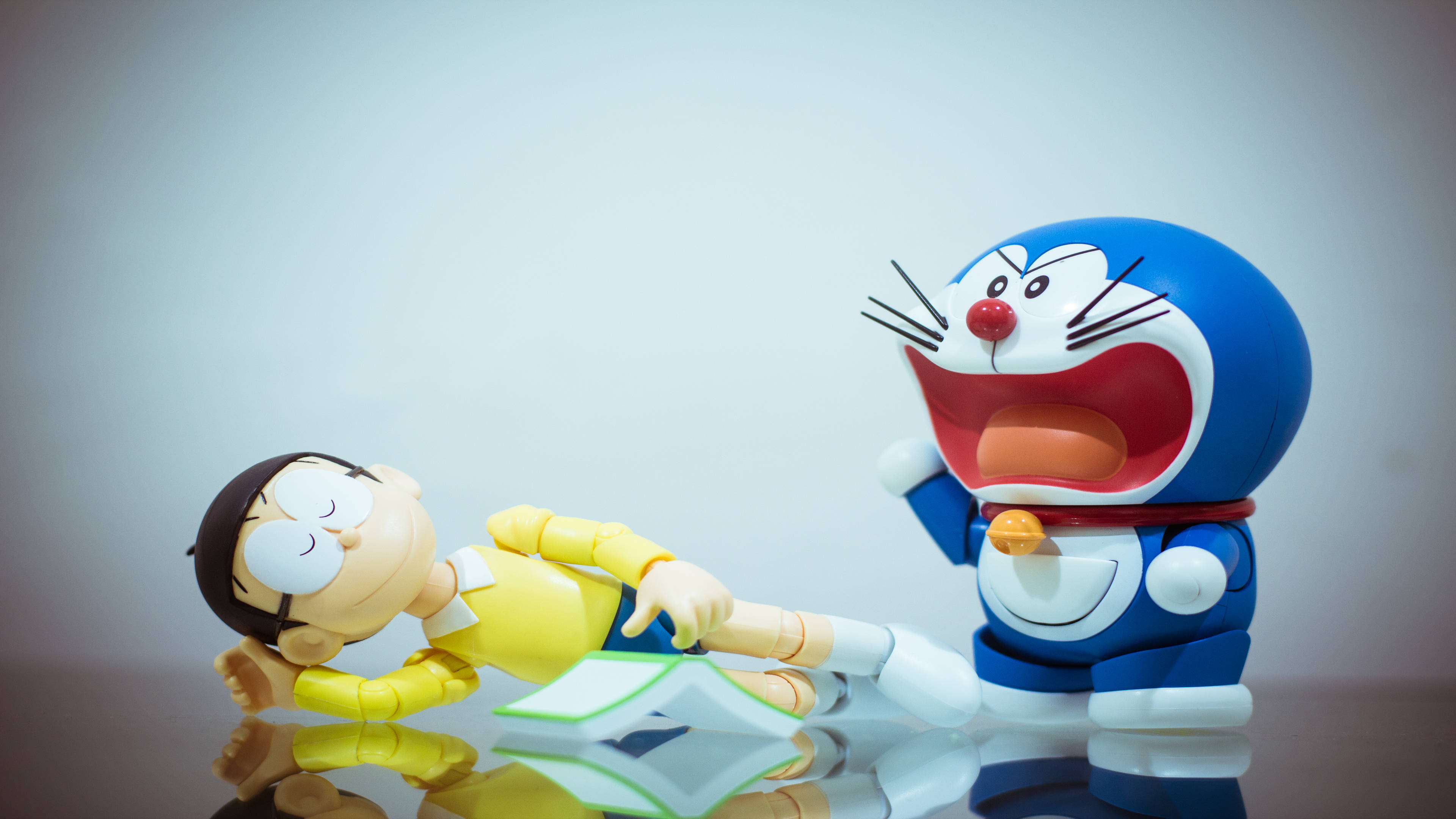Doraemon 桌布 壁紙 — 多啦A夢和大雄的模型在反光表面上戲劇性地擺姿勢，一個角色在笑，另一個躺著。