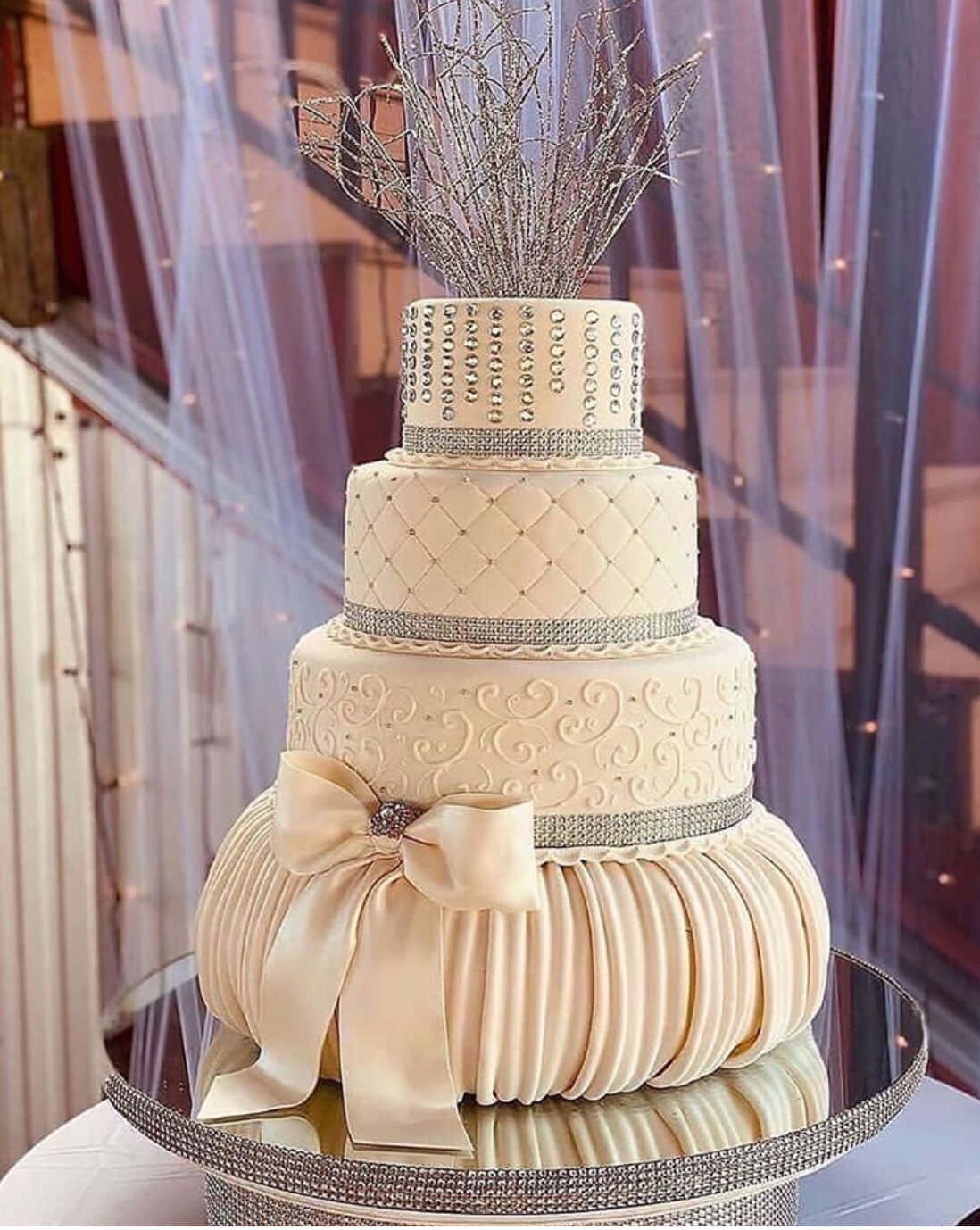 Wedding Cake 桌布 壁紙 — 多層象牙色婚禮蛋糕，飾有銀色水鑽褶皺和一個大蝴蝶結，優雅地放置在鏡面架上。