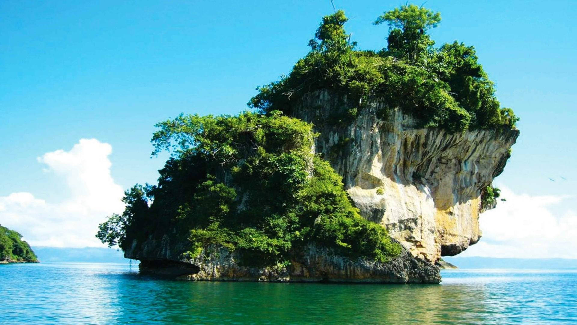多明尼加共和國岩石島嶼 壁紙 — 一個鬱鬱蔥蔥的綠色島嶼，岩石峭壁在清澈的藍天下從碧綠的海水中戲劇性地升起。