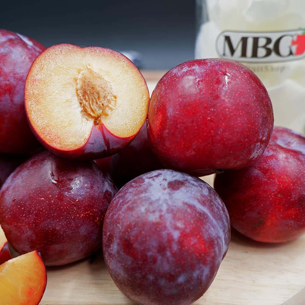 Red Plum 桌布 壁紙 — 多汁嘅布冧，有深紅色嘅皮同金色嘅果肉，堆喺木板上，背景有樽嘢。