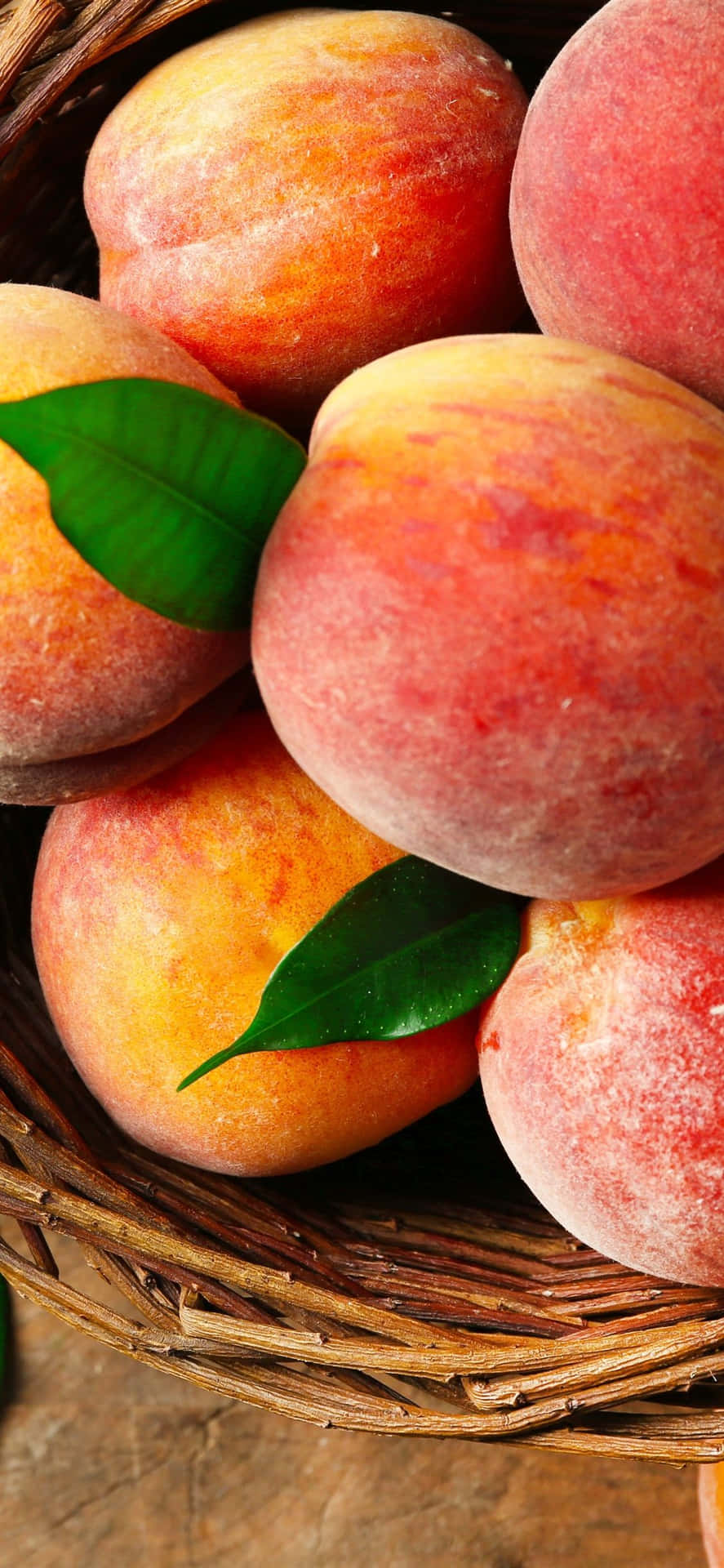 Peach iPhone 桌布 壁紙 — 多汁成熟的桃子配綠葉，放在木質表面上的編織籃子裡。