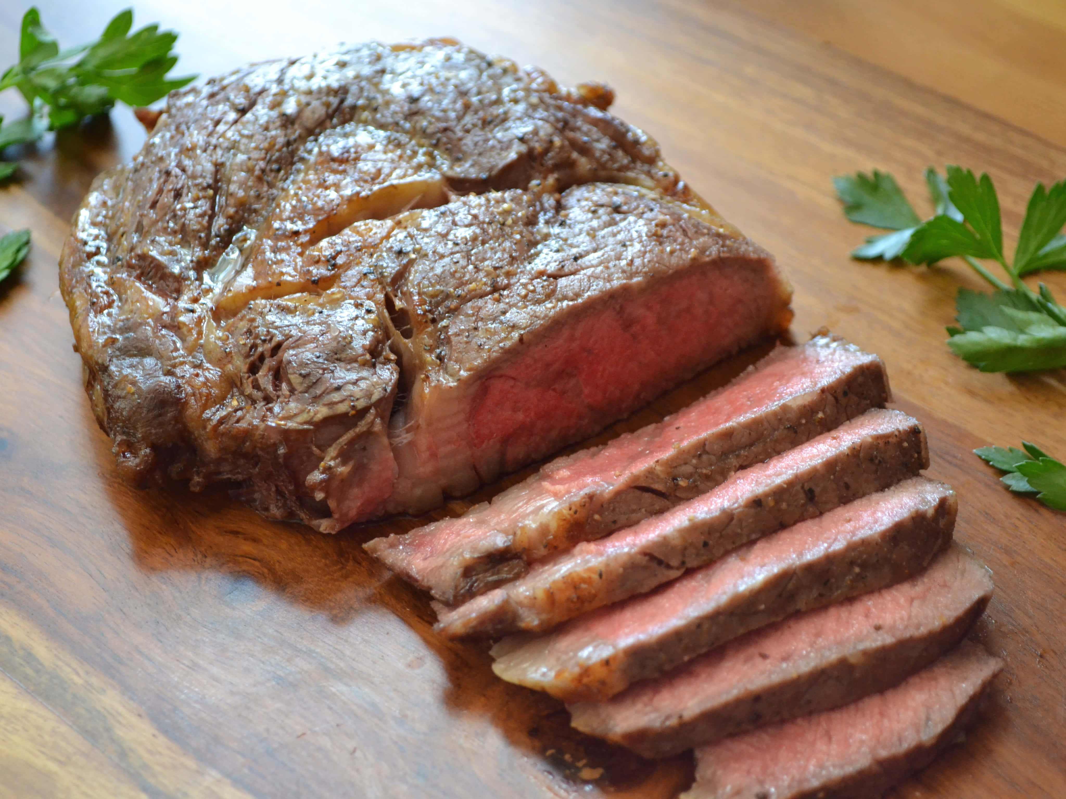 meat 桌布 壁紙 — 多汁的 medium-rare 烤牛肉，切片露出粉紅色中心，放在木砧板上，飾以新鮮歐芹。