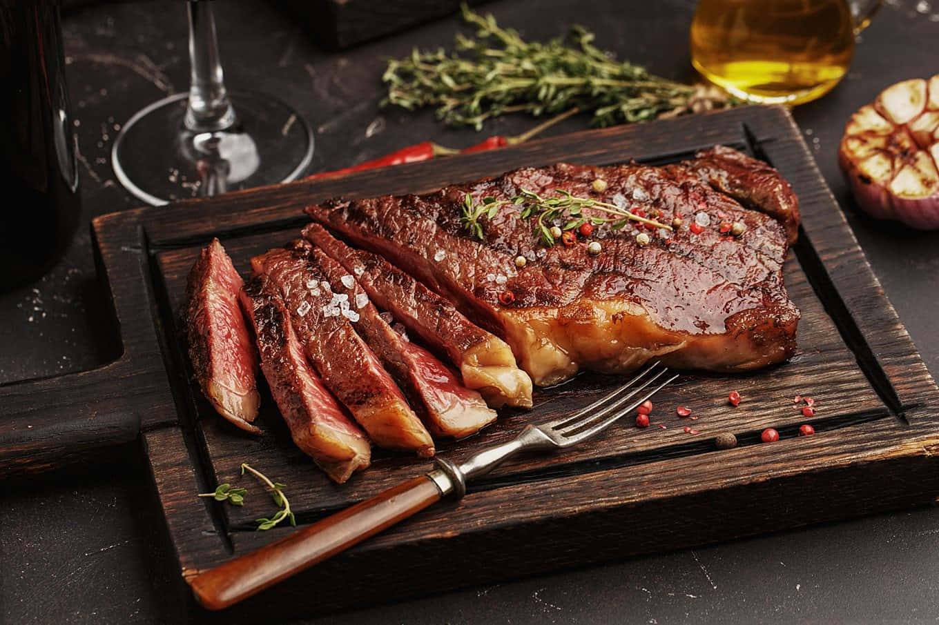 meat 桌布 壁紙 — 多汁的烤牛排切片放在質樸的木板上，配以香草、鹽和烤大蒜，旁邊放著一杯葡萄酒。