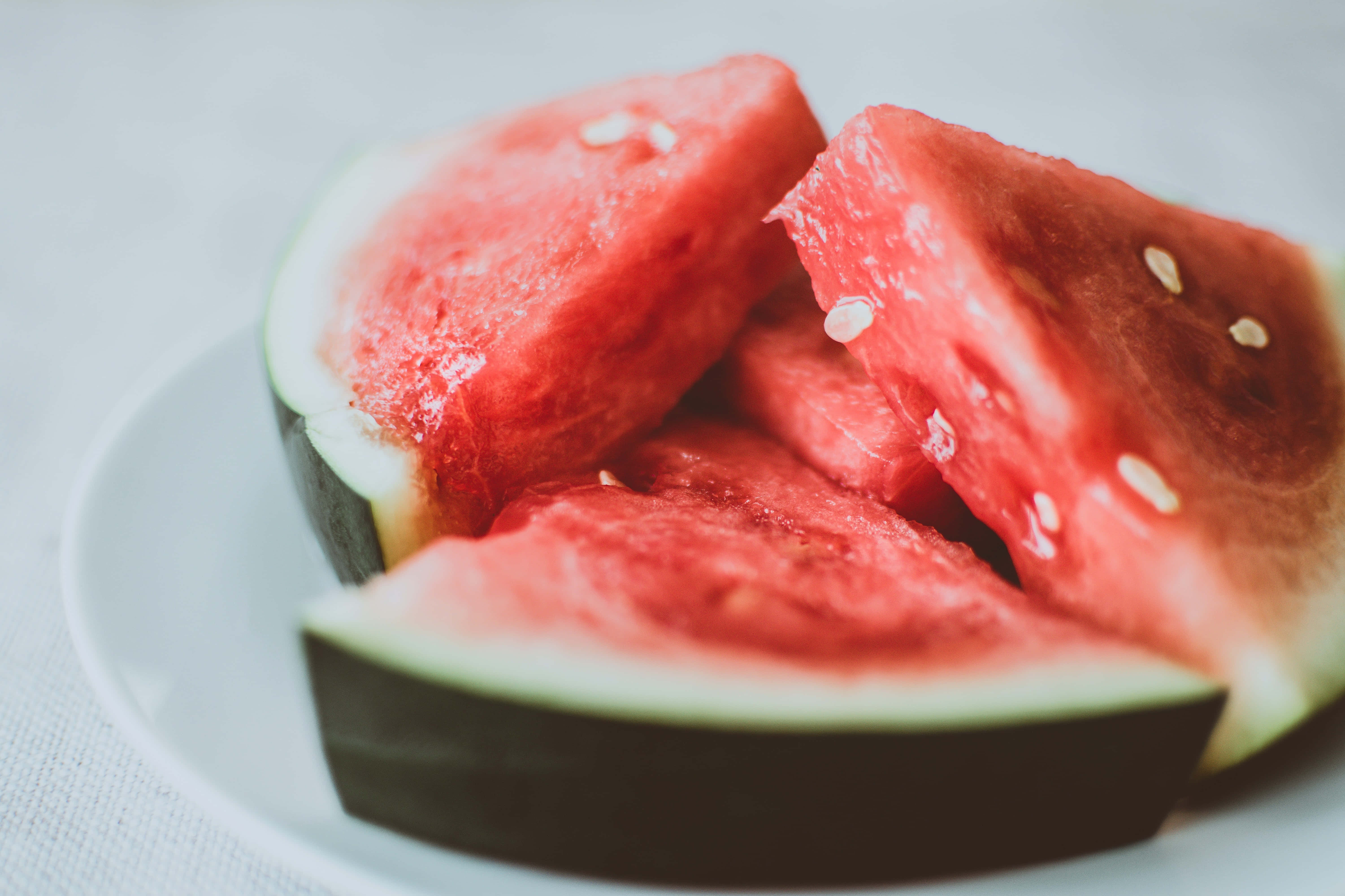 Summer Fruits 桌布 壁紙 — 多汁的紅西瓜片帶有黑色種子，放在白色盤子上，背景是柔和的灰色。