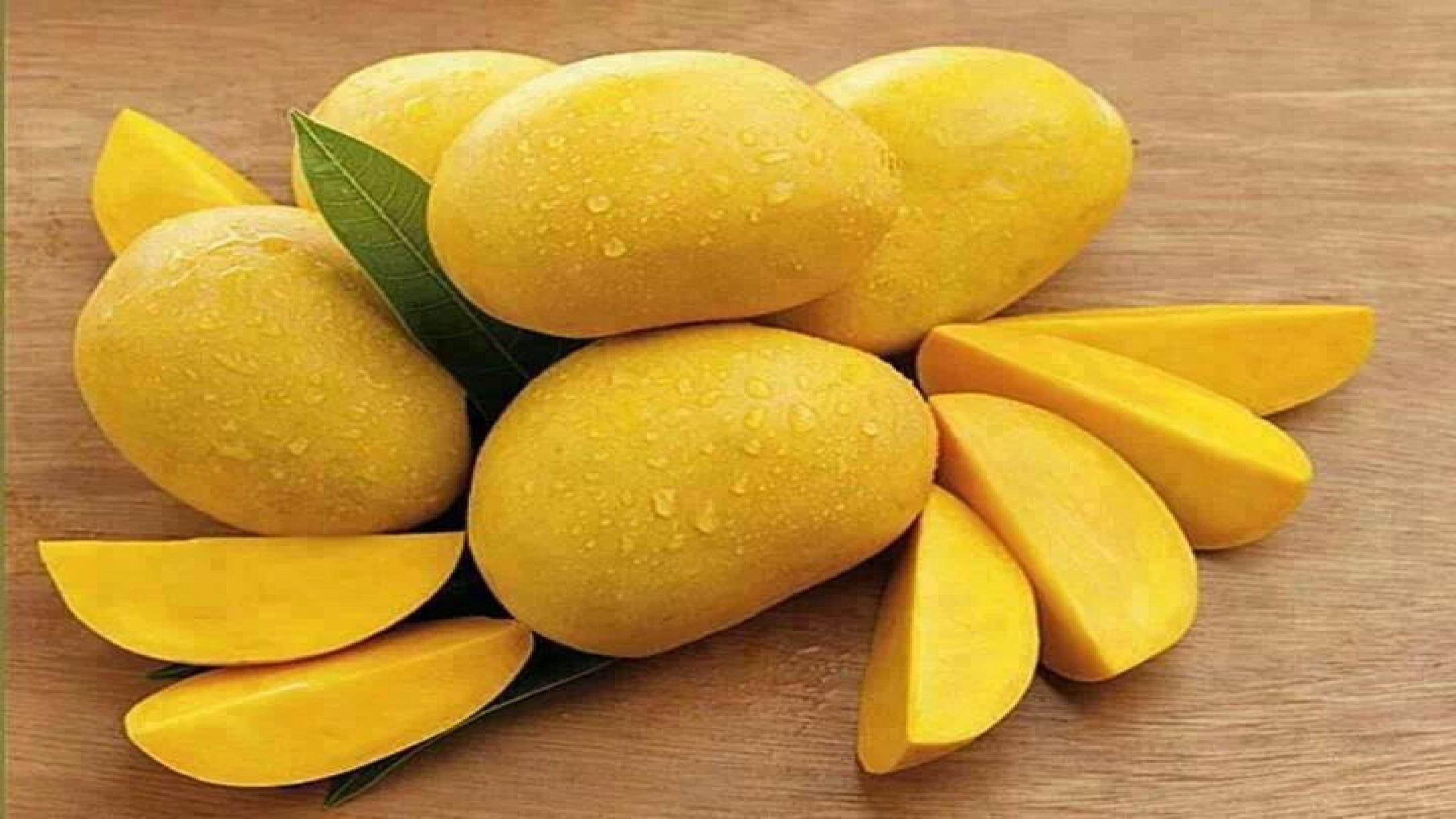 Mango 桌布 壁紙 — 多汁的黃色芒果，完整和切片，在溫暖的木質表面上閃爍著水滴。