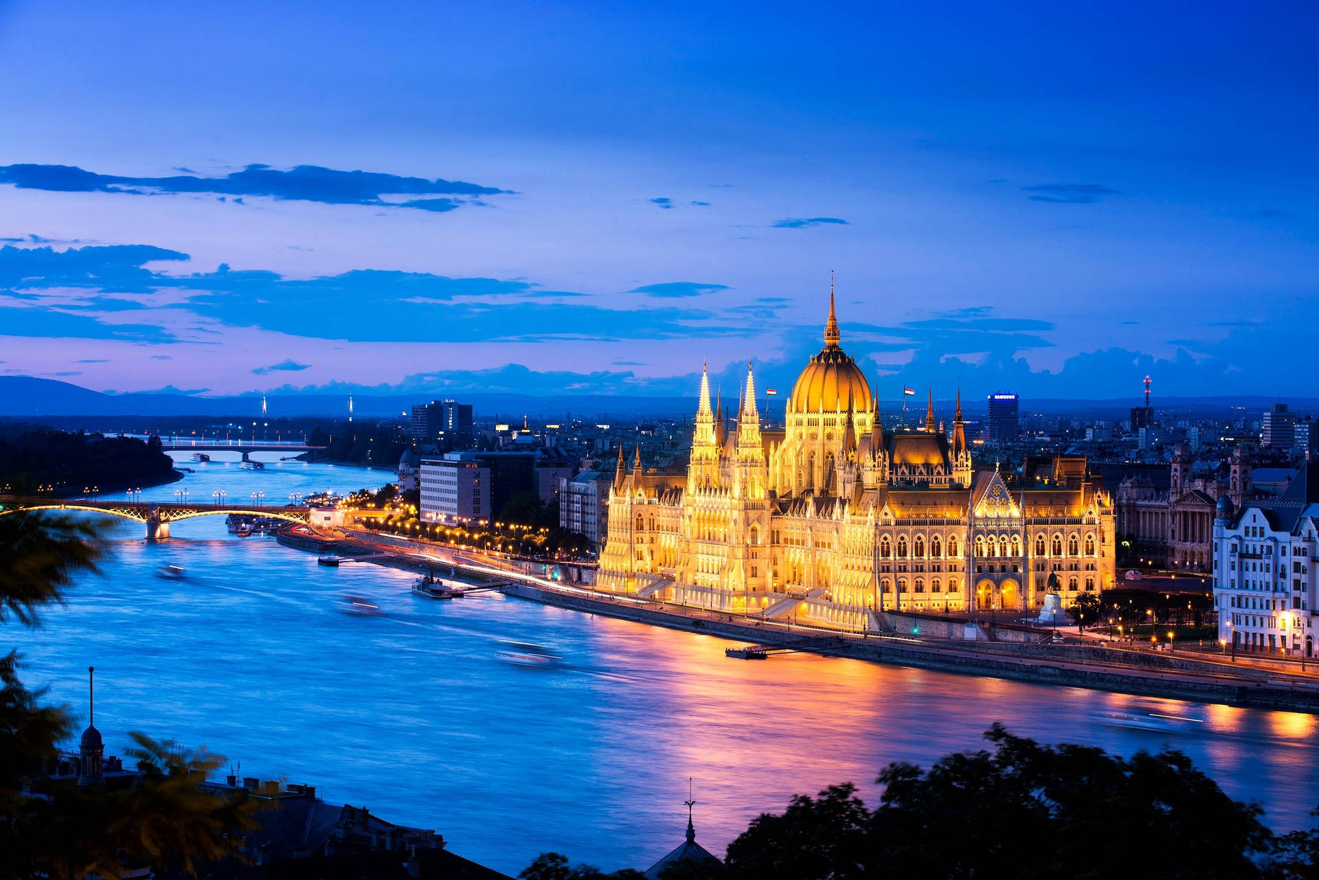 匈牙利國會大廈在黃昏時分於多瑙河畔亮起燈光，城市燈光倒映在水面上。