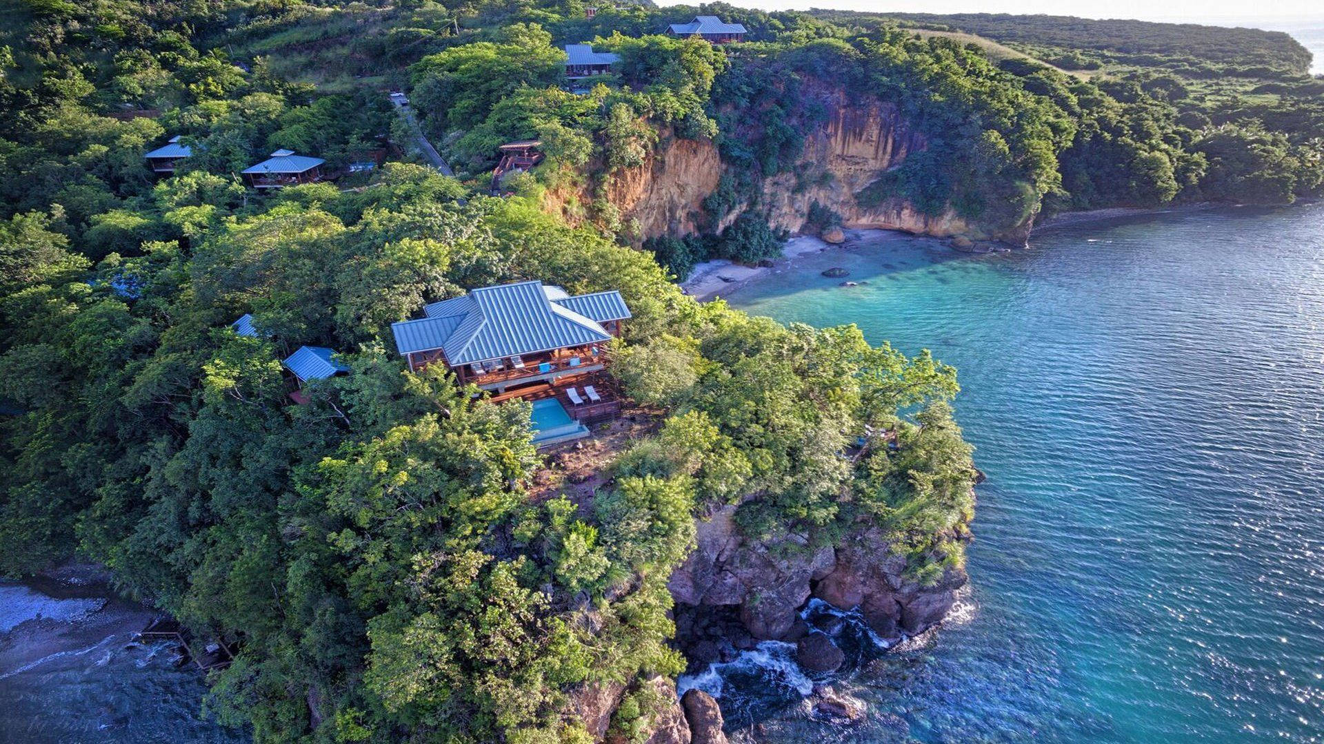 多米尼克島懸崖上的房屋 壁紙 — 俯瞰豪華懸崖別墅，坐落在茂密綠植中，俯瞰碧藍海水。