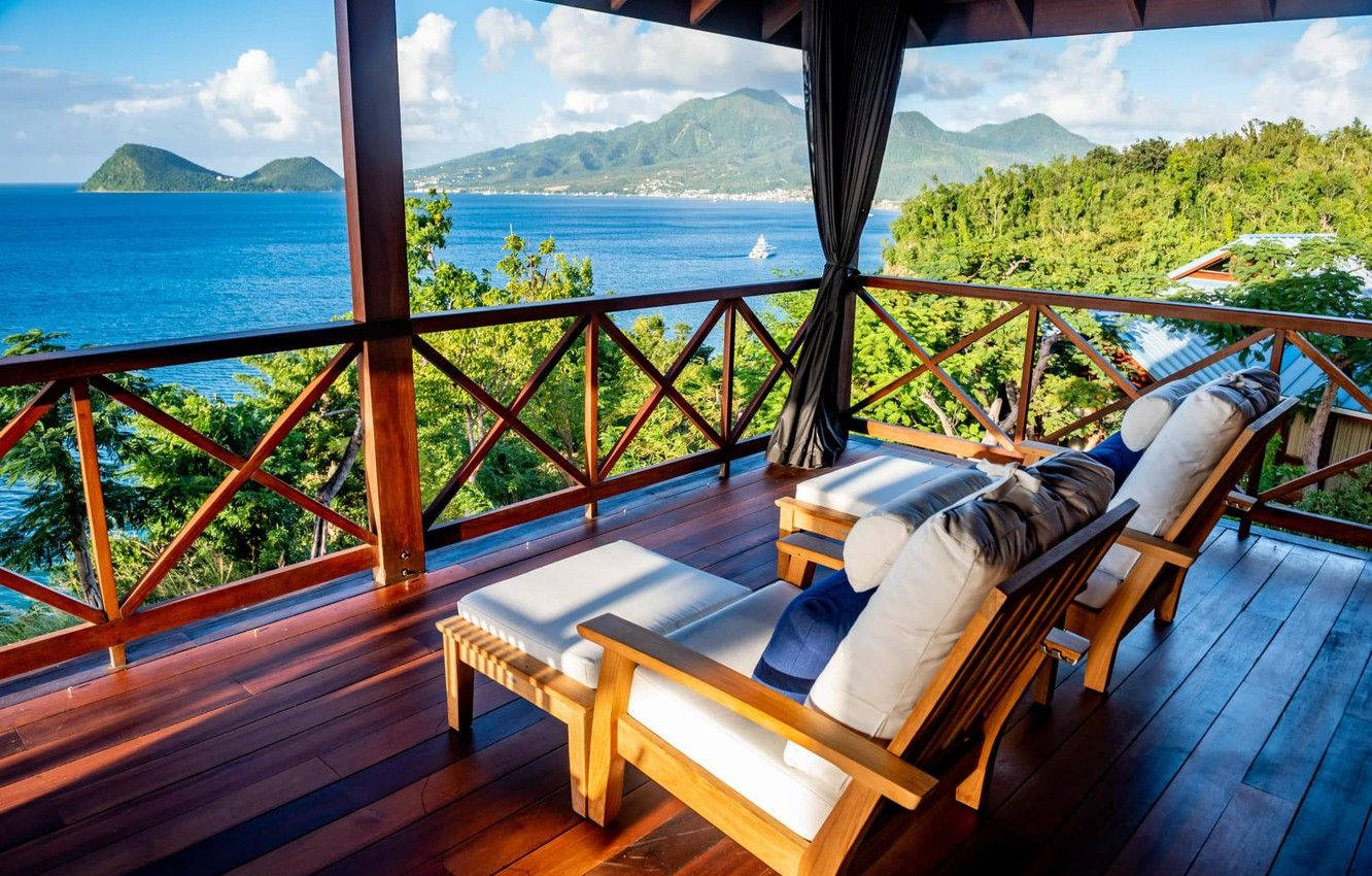 多米尼克島海景木屋 壁紙 — 豪華木甲板配備躺椅，俯瞰碧綠海洋和鬱鬱蔥蔥的青山，在晴朗陽光下。