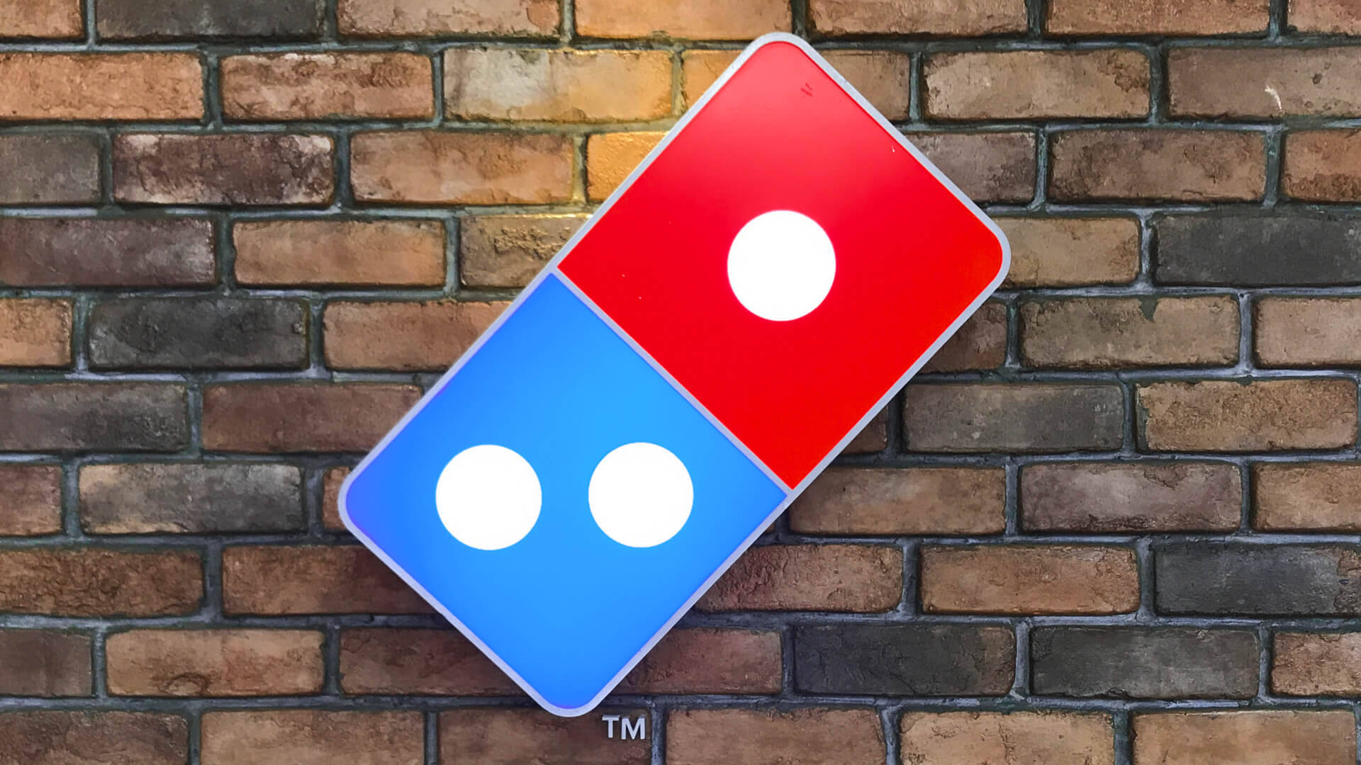 多米諾披薩標誌掛於磚牆 壁紙 — 一個紅藍色的 Domino's pizza 標誌牌靠在風化的磚牆上。