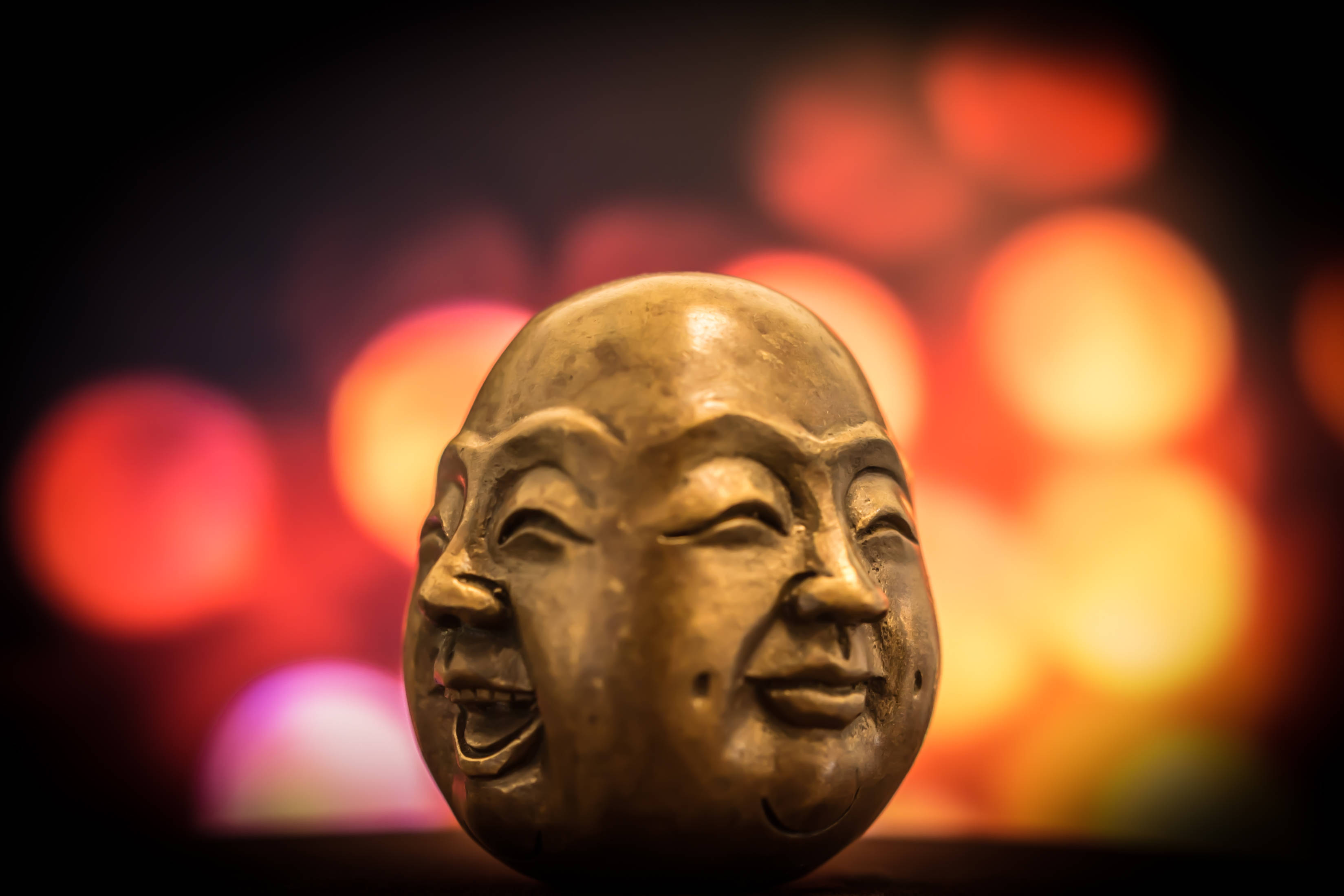 多面石雕假笑 壁紙 — 一個金色的笑佛頭像雕塑在紅色和橙色燈光的溫暖散景背景下閃耀。