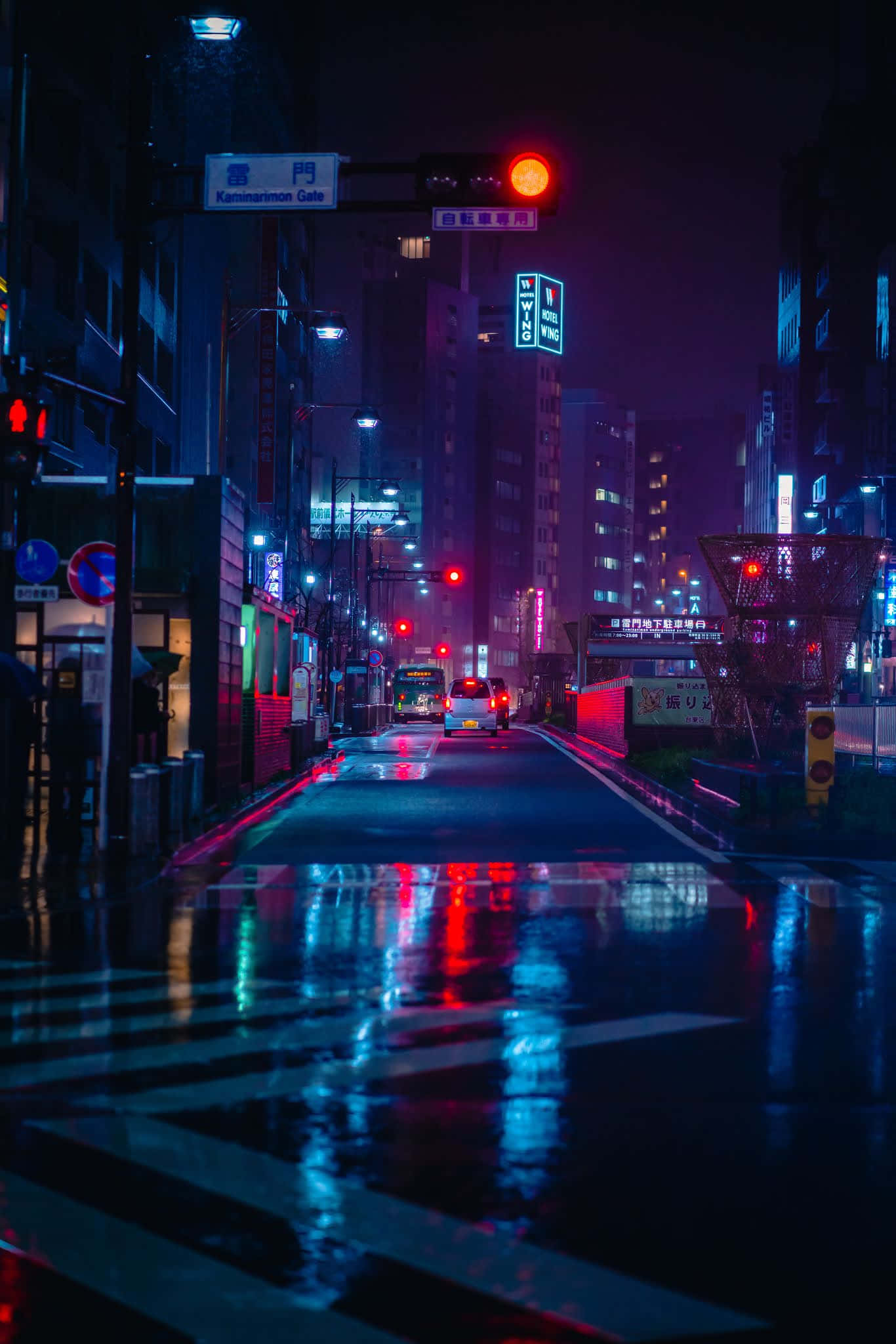 夜之城的明亮燈光 壁紙 — 一條被雨水浸濕、霓虹燈閃爍的東京街道在夜晚反射出交通信號燈和招牌上鮮豔的紅藍燈光。