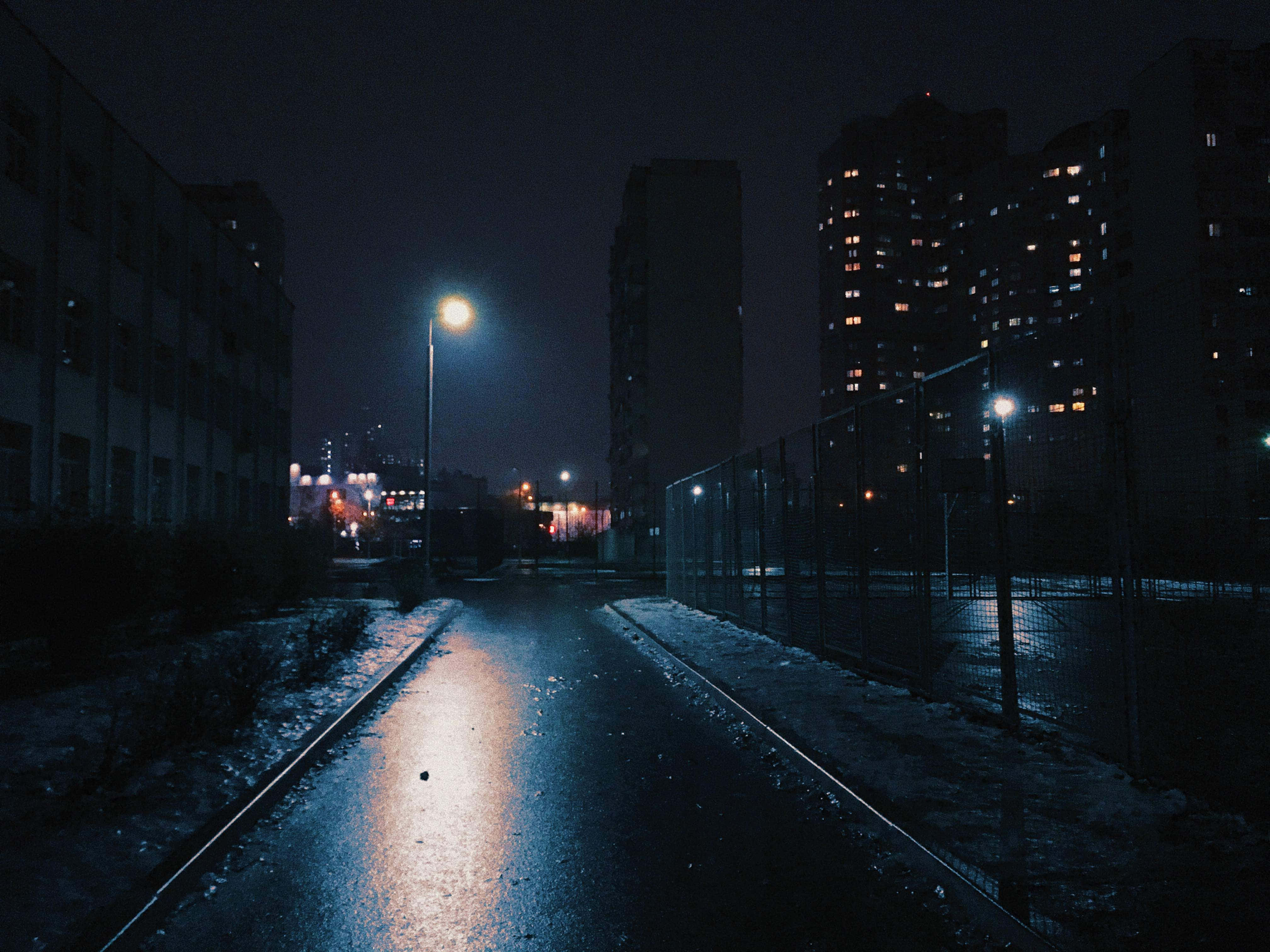 夜城壯闊的城市景觀 壁紙 — 夜晚濕漉漉的城市小巷，在黑暗的天空下反射出路燈和遠處建築物的窗戶。