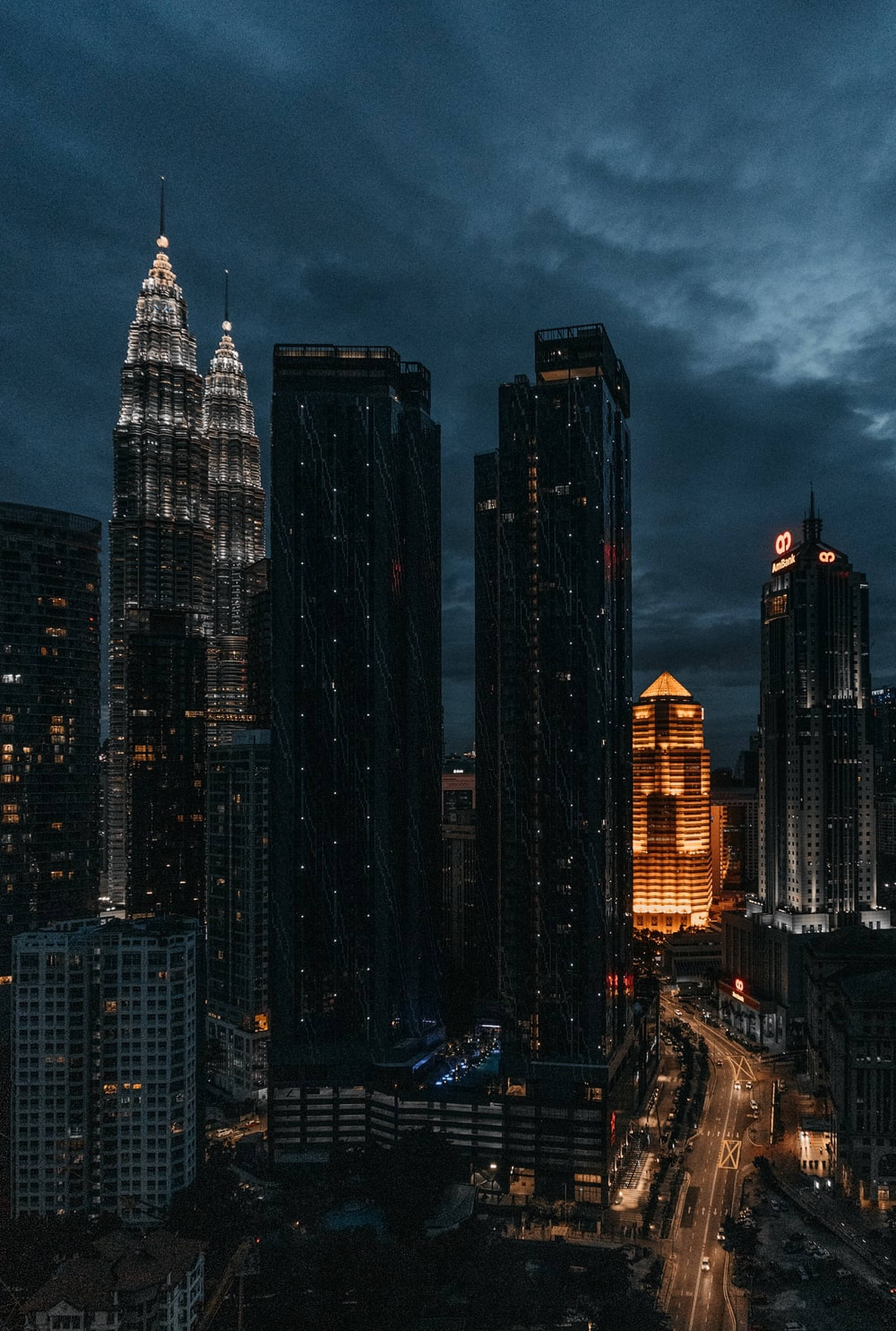 夜幕下的城市摩天大樓 壁紙 — 高聳的摩天大樓刺穿陰沉的暮色天空，城市燈光在下方密集的城市峽谷中閃爍。