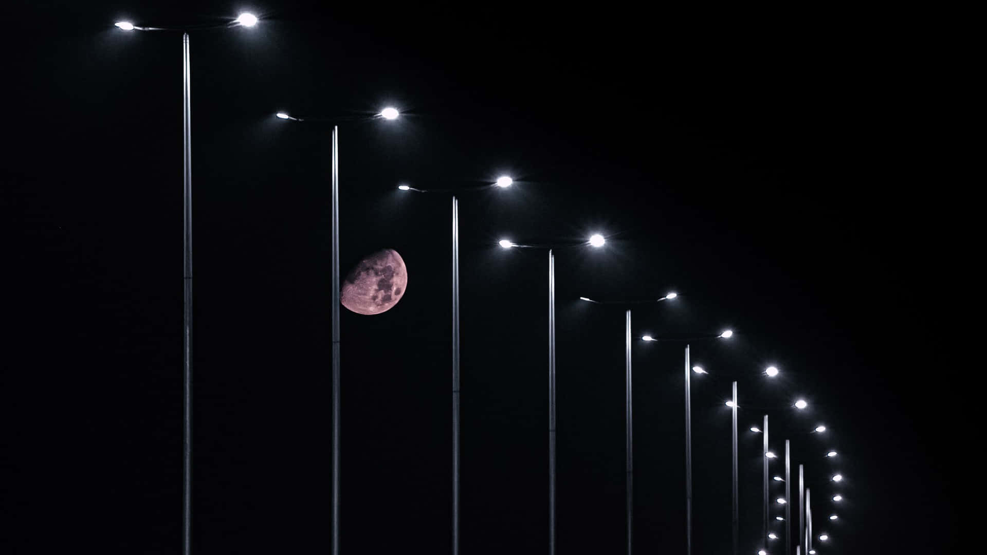 夜晚，彎曲街燈列後方可見粉紅色月亮。