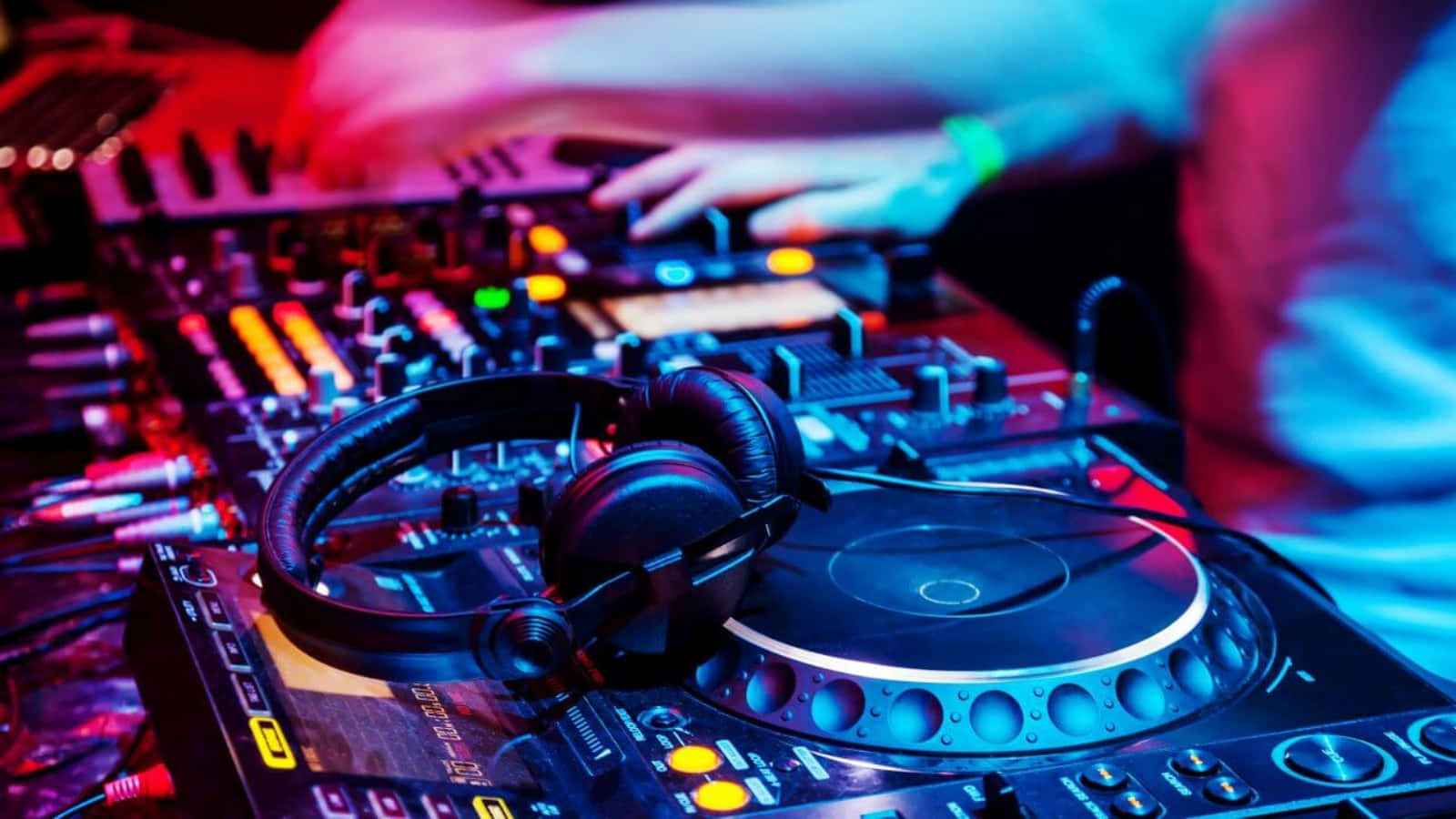 夜店DJ音樂設置圖片 壁紙 — DJ嘅手喺充滿活力嘅紅色同藍色俱樂部燈光下，喺發光嘅唱盤上混音，耳機就放喺附近。