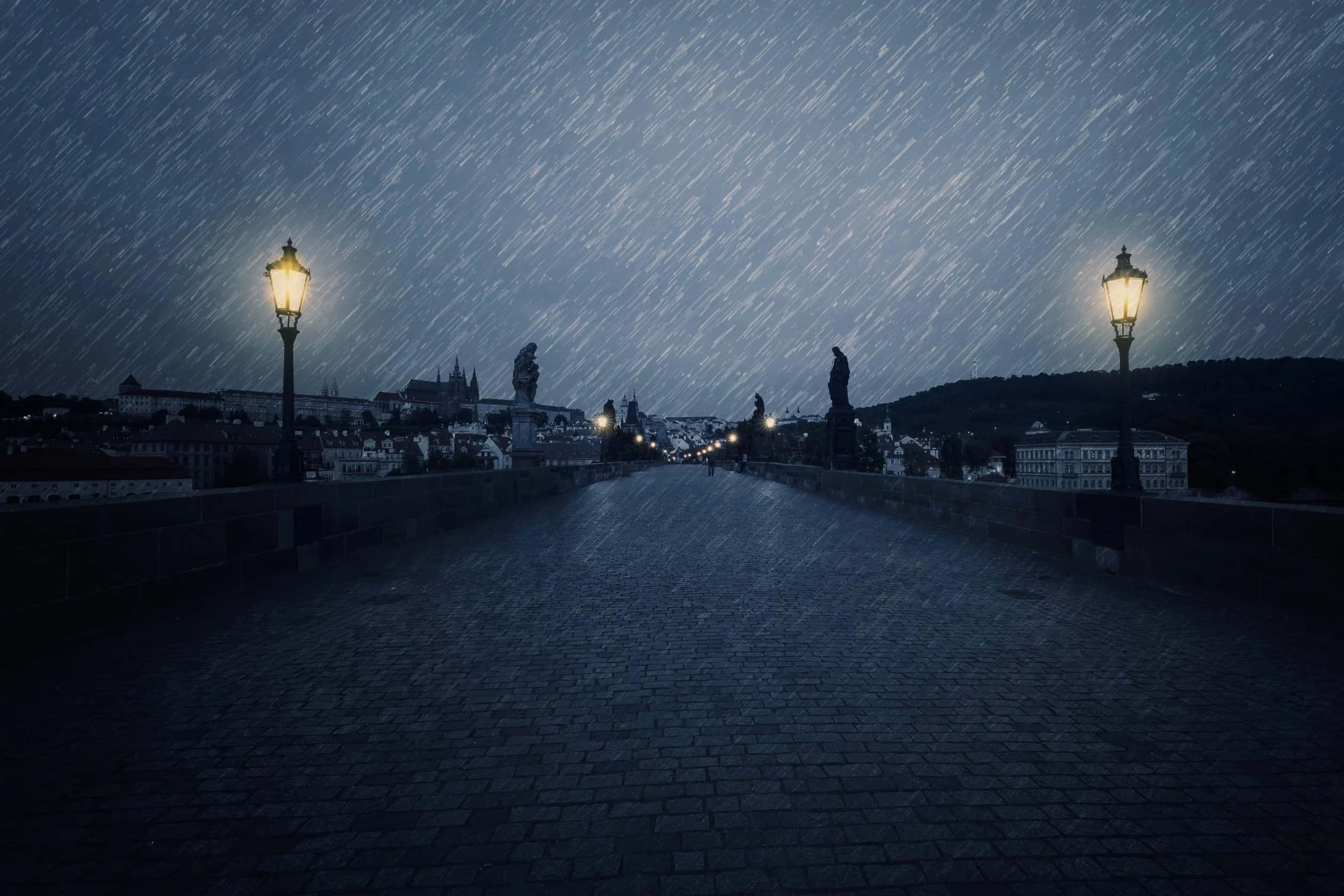 Raining 桌布 壁紙 — 夜晚，一條被雨水打濕的鵝卵石橋，發光的街燈和雕像在暴風雨的天空下形成剪影。