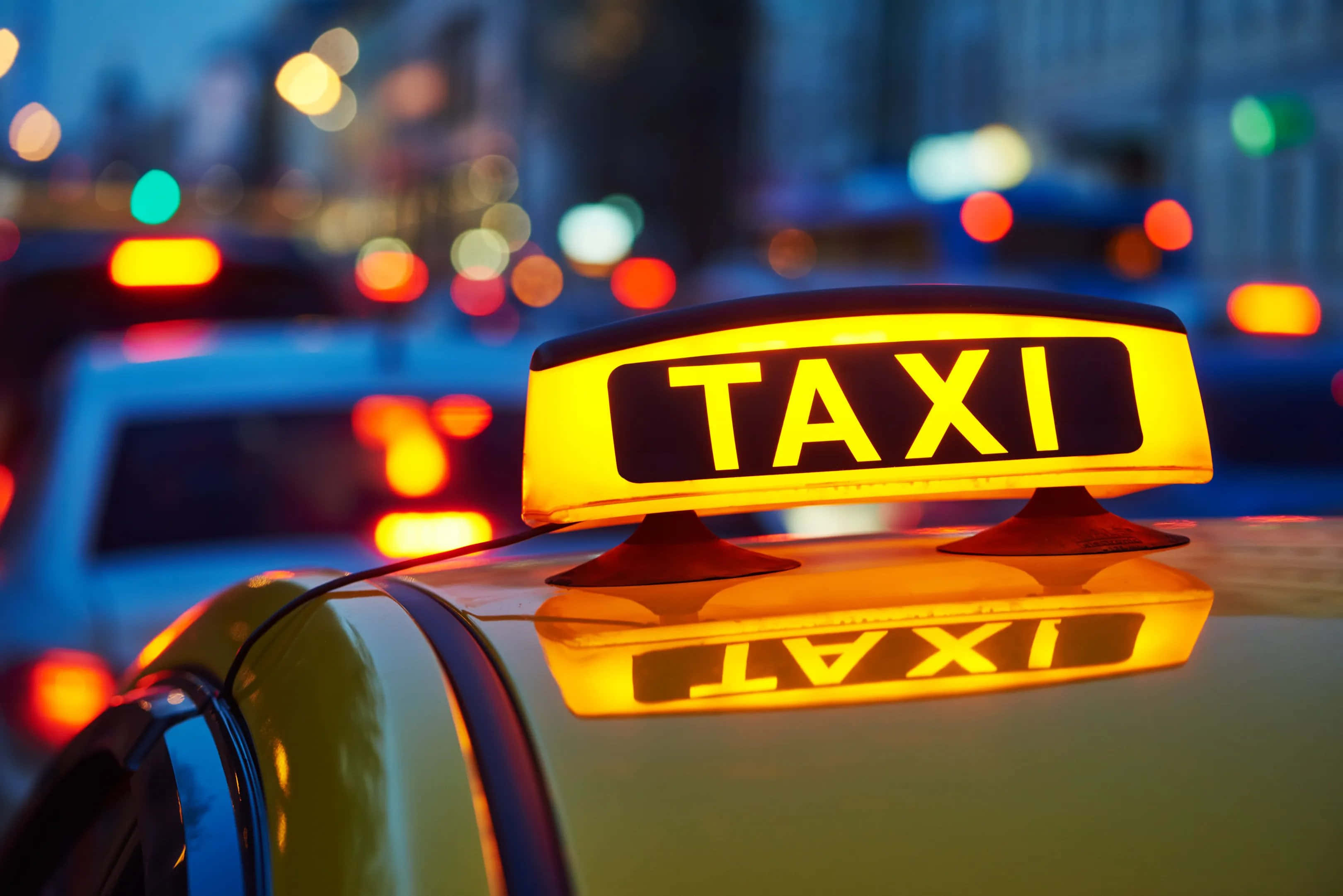taxi 桌布 壁紙 — 夜晚，一輛的士頂上發光的黃色的士標誌，背景是模糊的城市燈光。