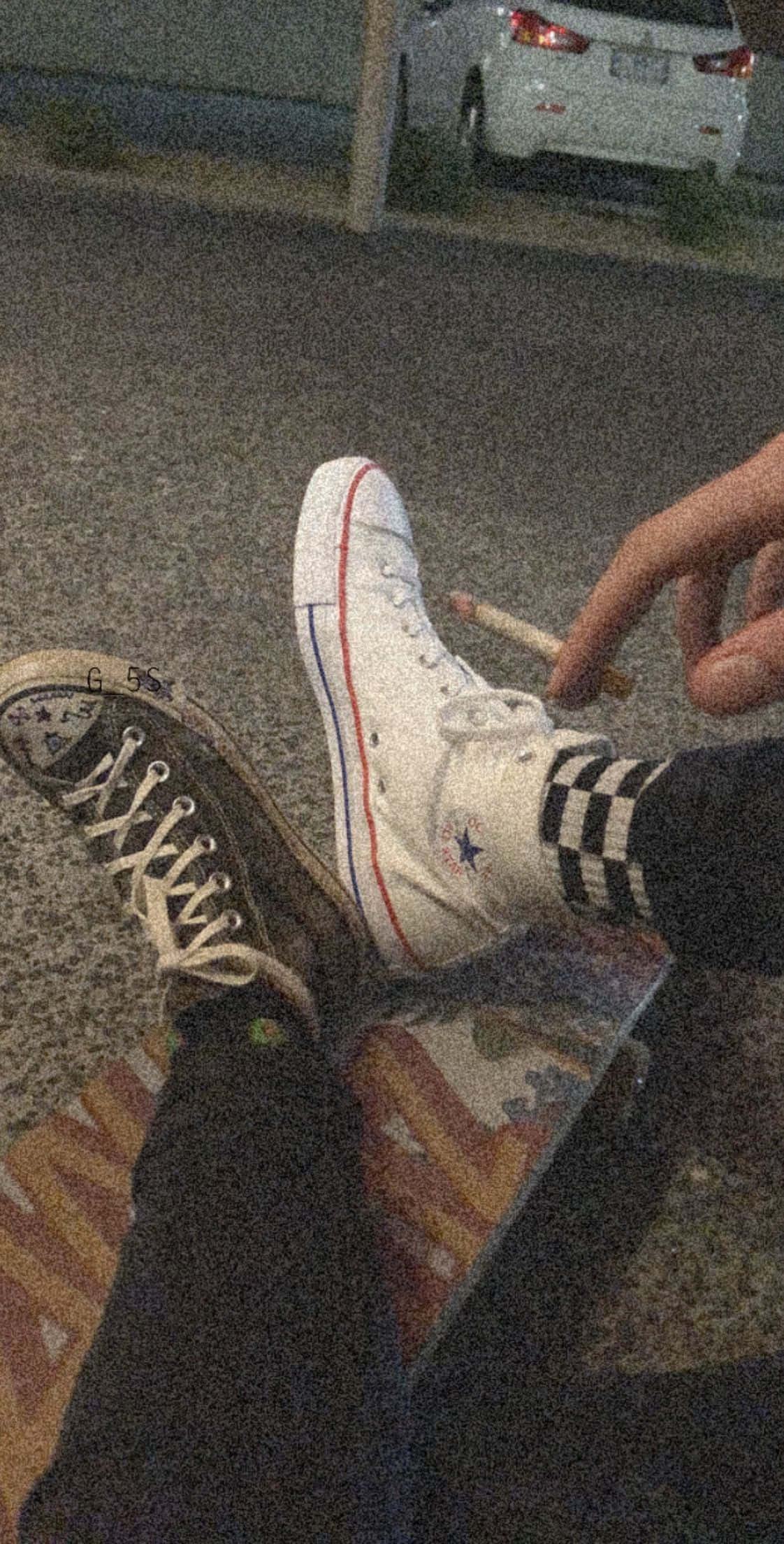 滑板少年美學 桌布 壁紙 — 夜晚，一雙穿著對比鮮明黑白運動鞋的腳踏在滑板上，手持香煙的特寫。