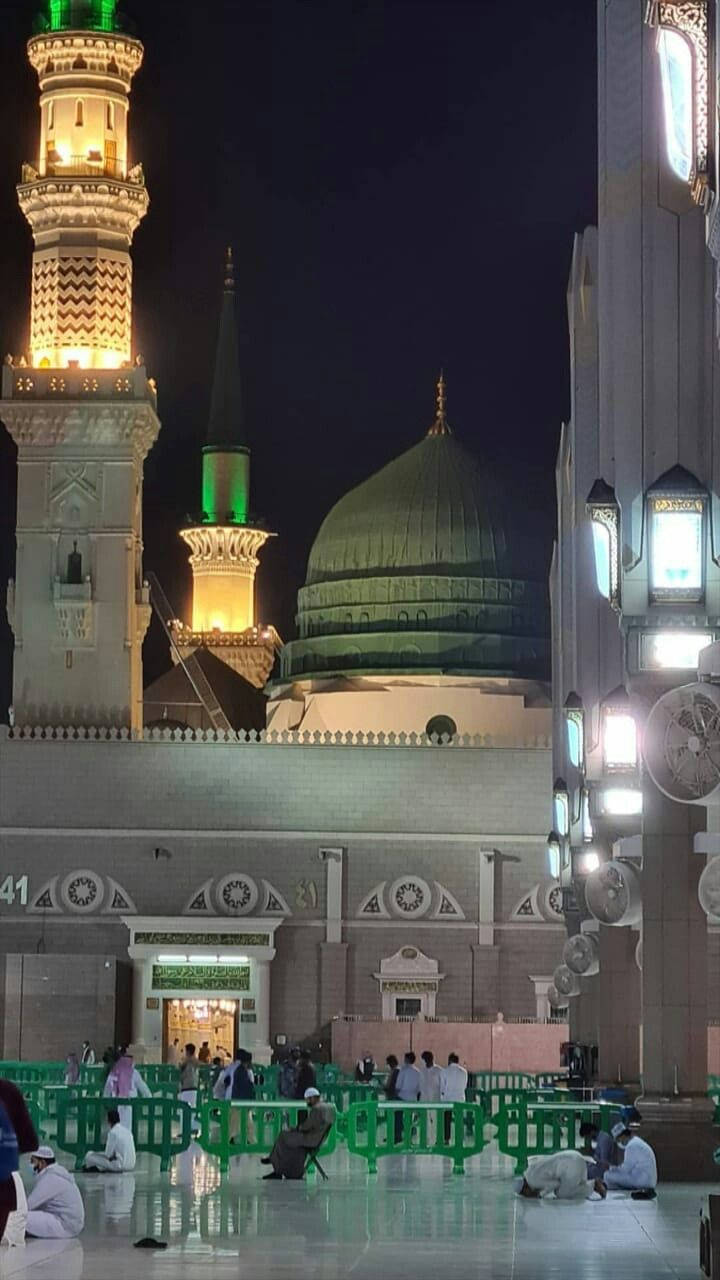 Madina Sharif 桌布 壁紙 — 夜晚，信徒在反光大理石地板上祈禱，綠色圓頂和宣禮塔閃閃發光的清真寺。