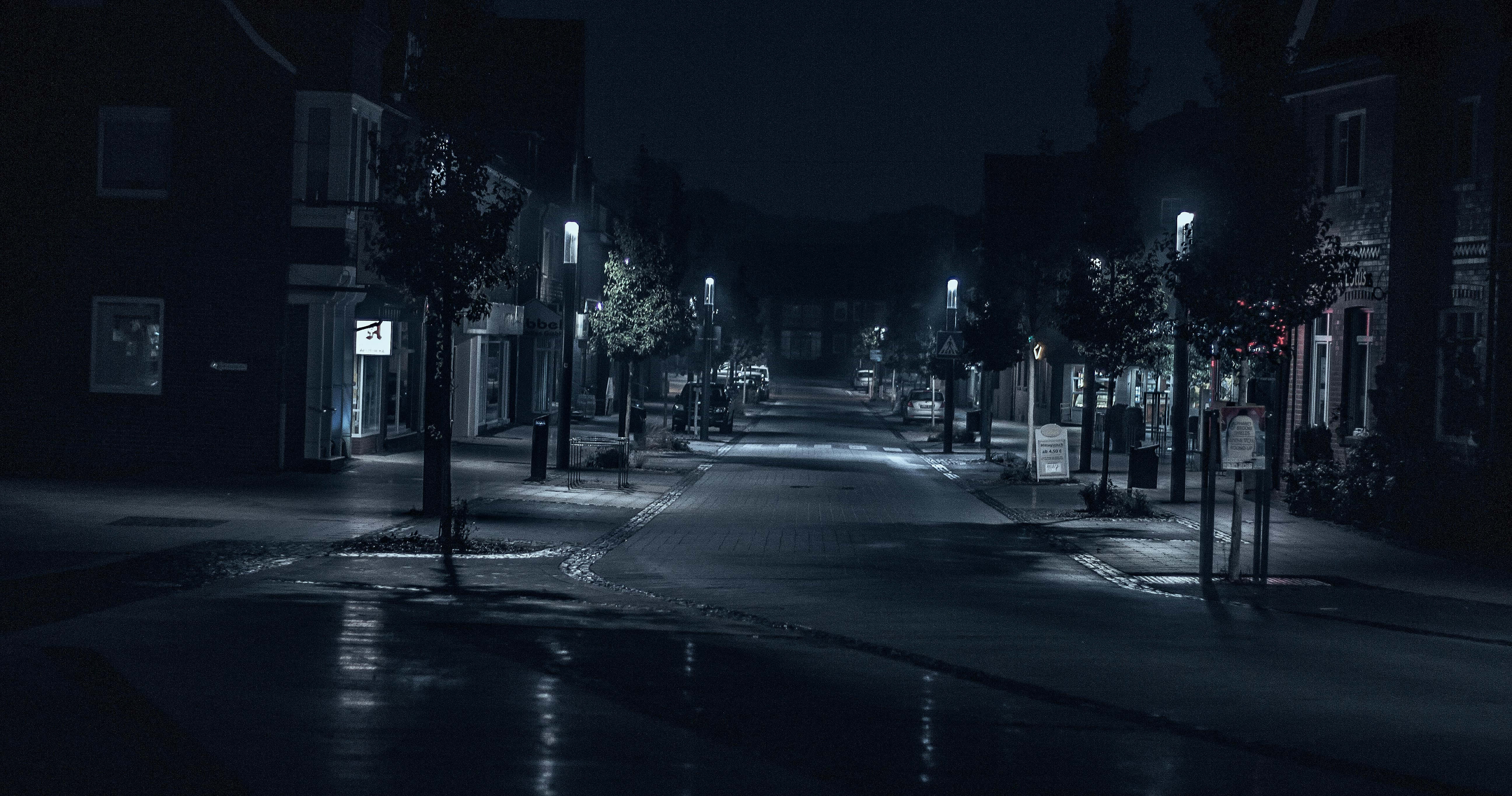 Night Street 桌布 壁紙 — 夜晚一條寧靜、被雨水打濕的城市街道，柔和的路燈在建築物之間投下長長的影子。