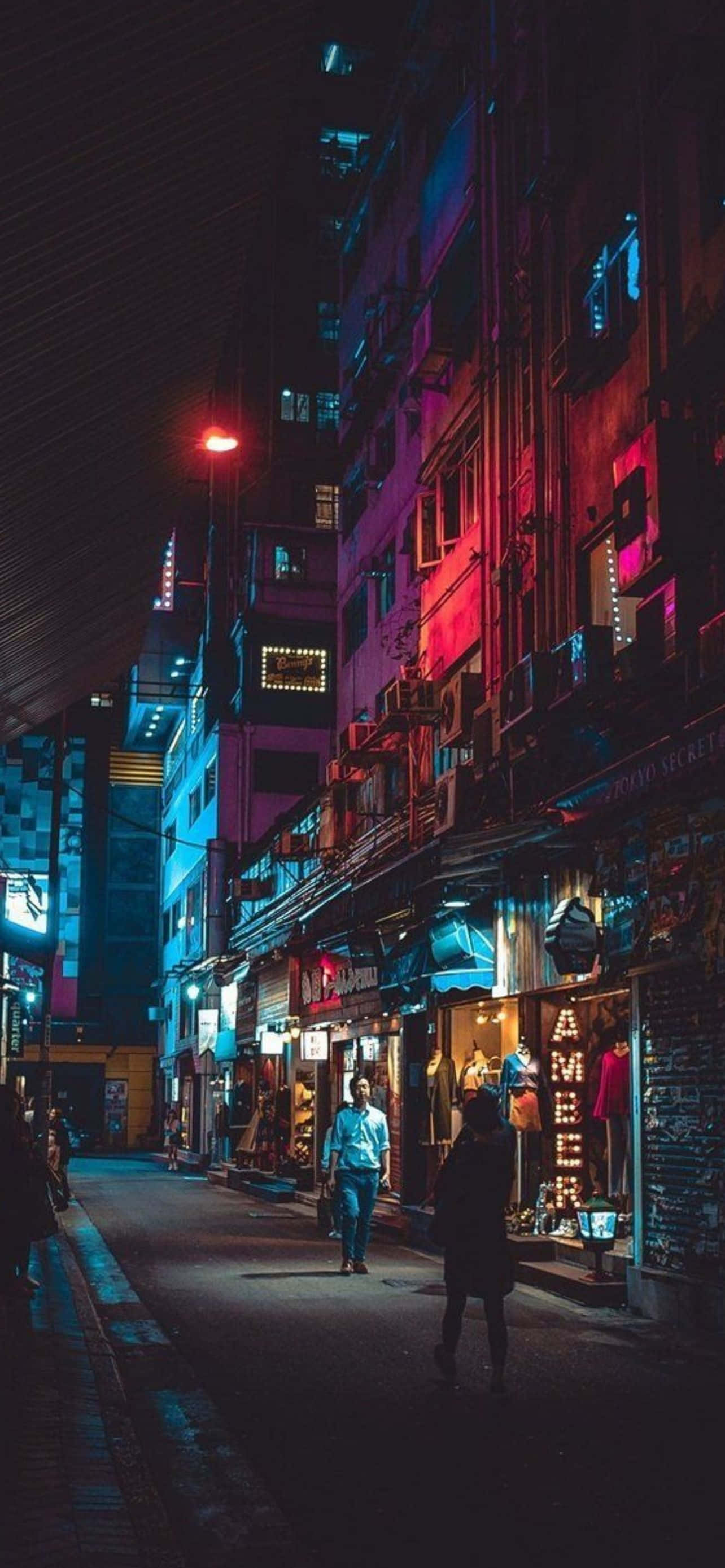 型格 iPhone 壁紙 桌布 壁紙 — 夜晚一條狹窄的霓虹燈小巷，行人走過色彩繽紛的商店櫥窗，頭頂是漆黑的天空。