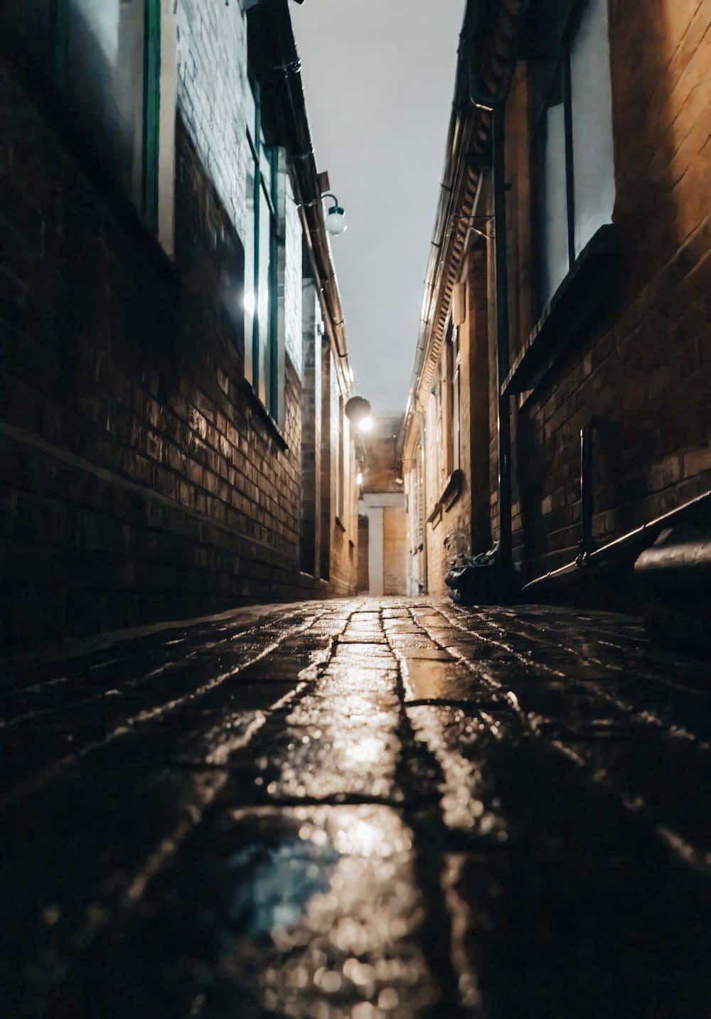 Dark Alleyway 桌布 壁紙 — 夜晚一條狹窄的鵝卵石小巷，濕漉漉的石頭在磚砌建築之間反射著溫暖的街燈。
