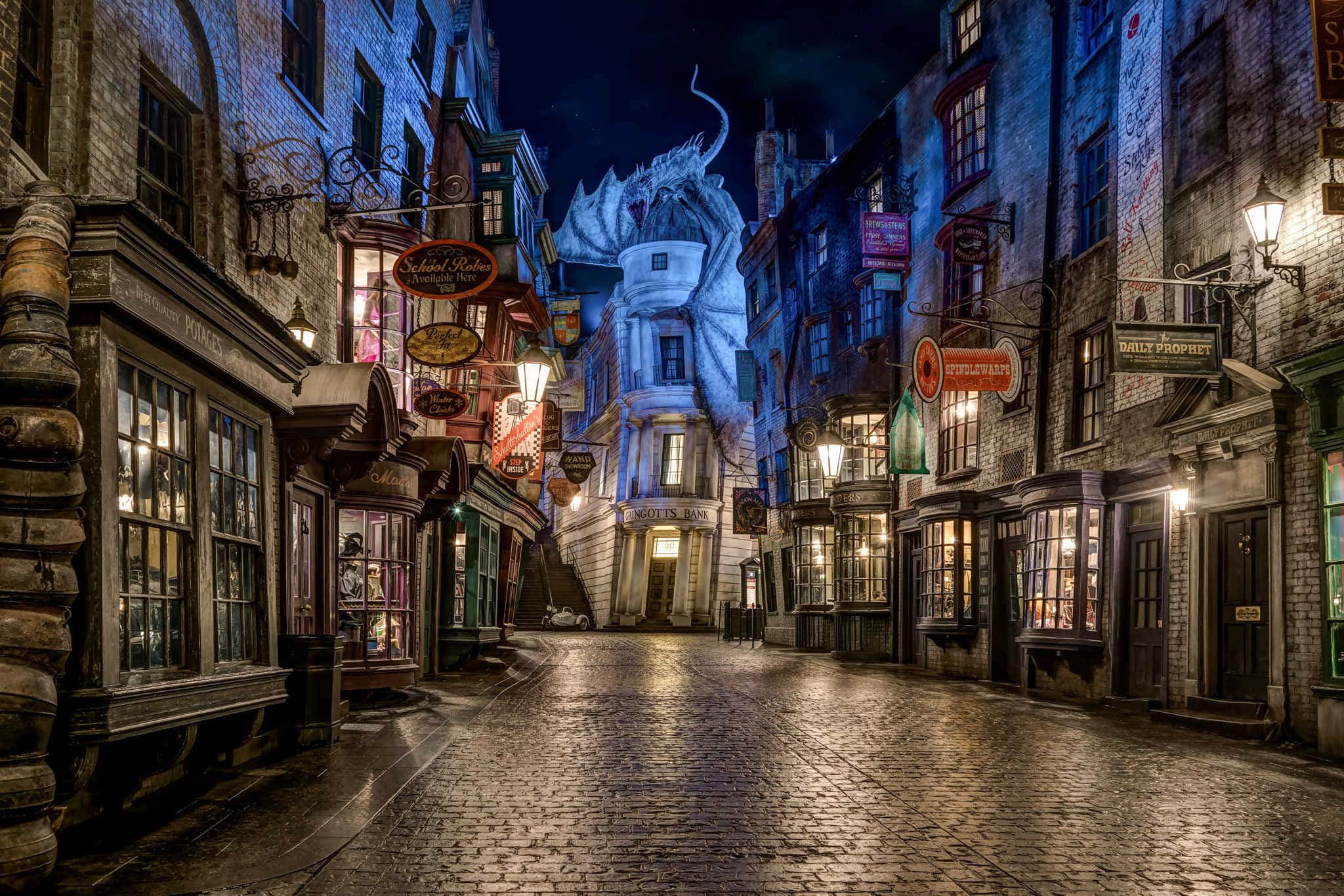 Diagon Alley 桌布 壁紙 — 夜晚一條神奇的鵝卵石街道，被溫暖的商店燈光和銀行上方高聳的龍雕塑照亮。