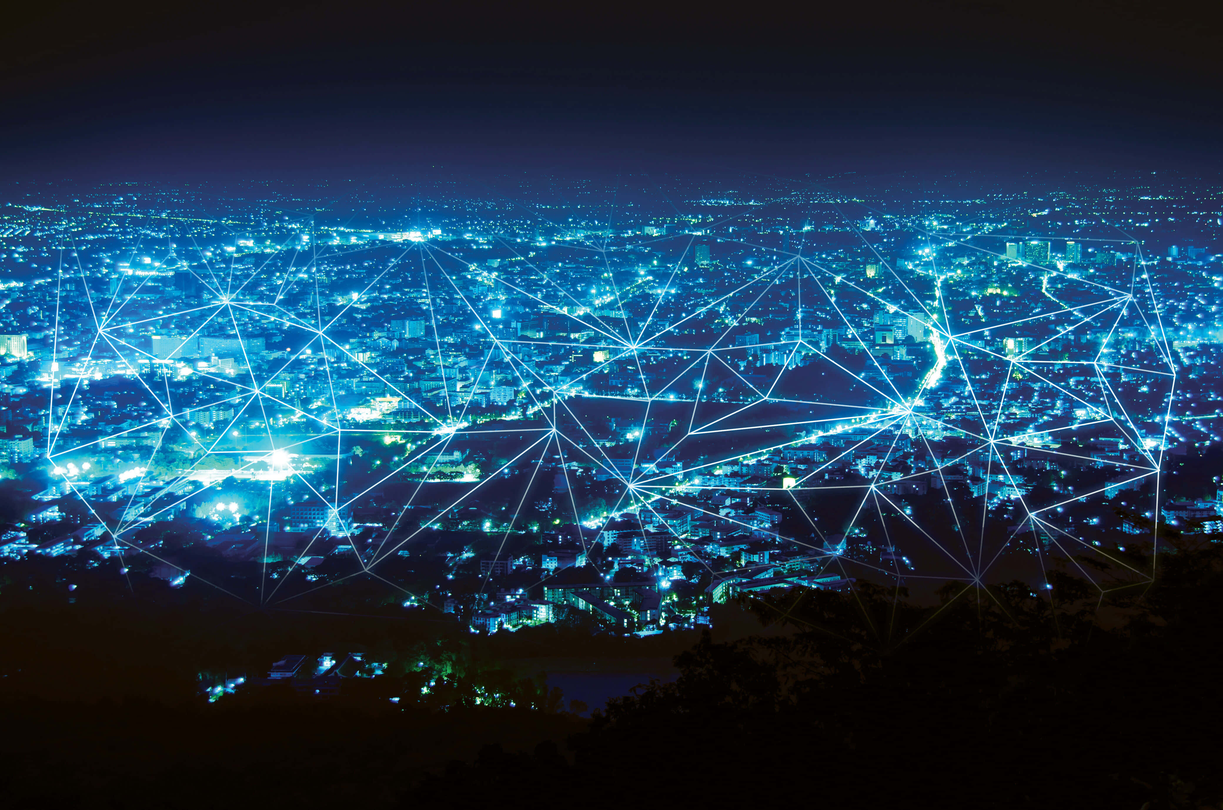 Internet 桌布 壁紙 — 夜晚中一座廣闊的城市被發光的藍色燈光照亮，並有數碼網絡覆蓋層連接建築物和街道。
