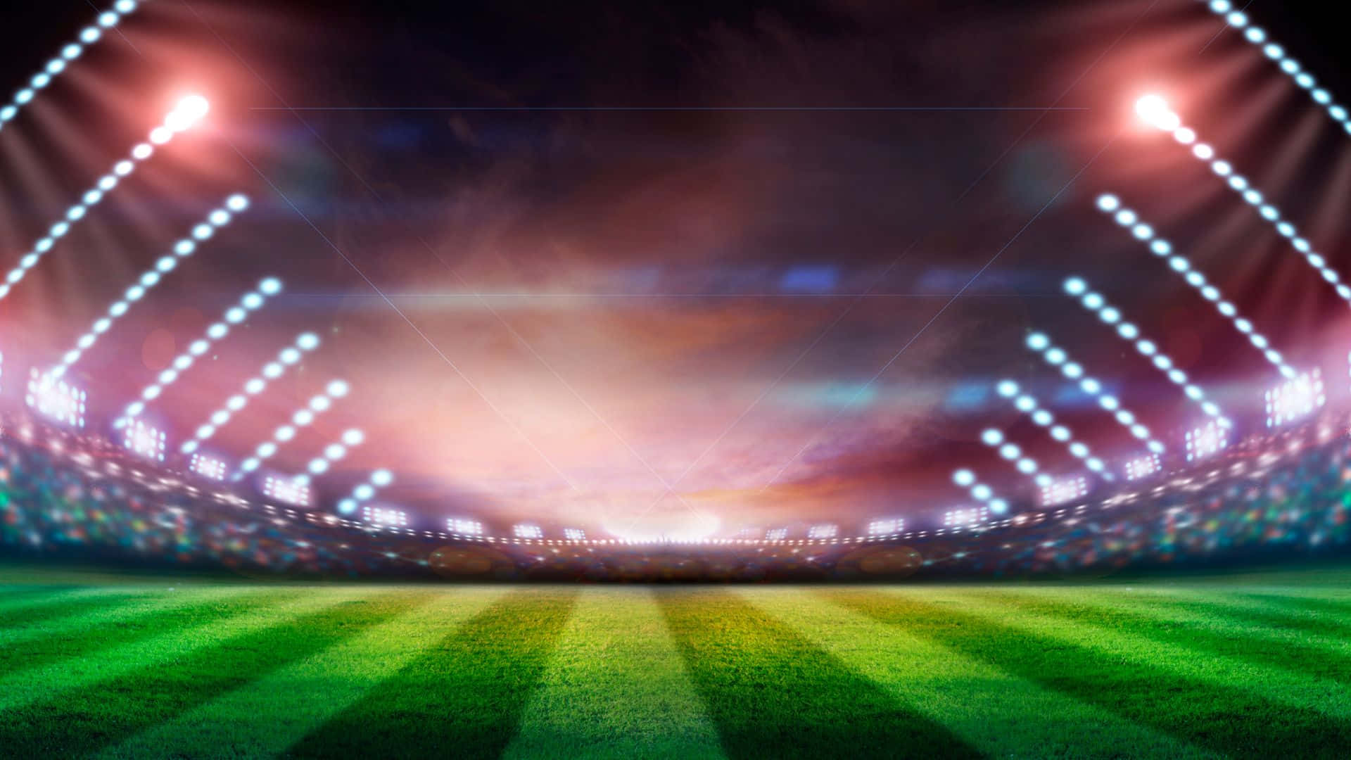 Soccer Stadium 桌布 壁紙 — 夜晚充滿活力的體育場，閃爍的泛光燈照亮了色彩繽紛天空下鬱鬱蔥蔥的綠色場地。