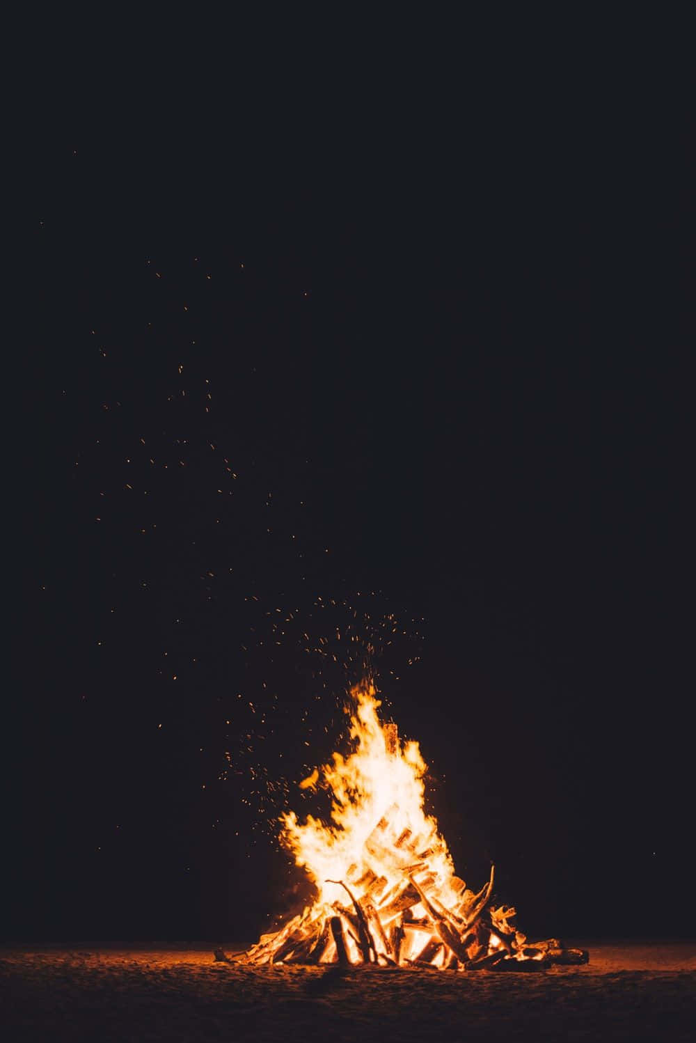 Beach Bonfire 桌布 壁紙 — 夜晚咆哮的營火將明亮的橙色火焰和發光的餘燼送向漆黑的天空。