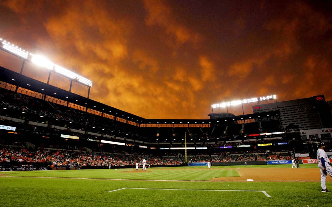 Baseball Stadium 桌布 壁紙 — 夜晚嘅棒球場，火橙色天空下，場上有球員，看台上有球迷。
