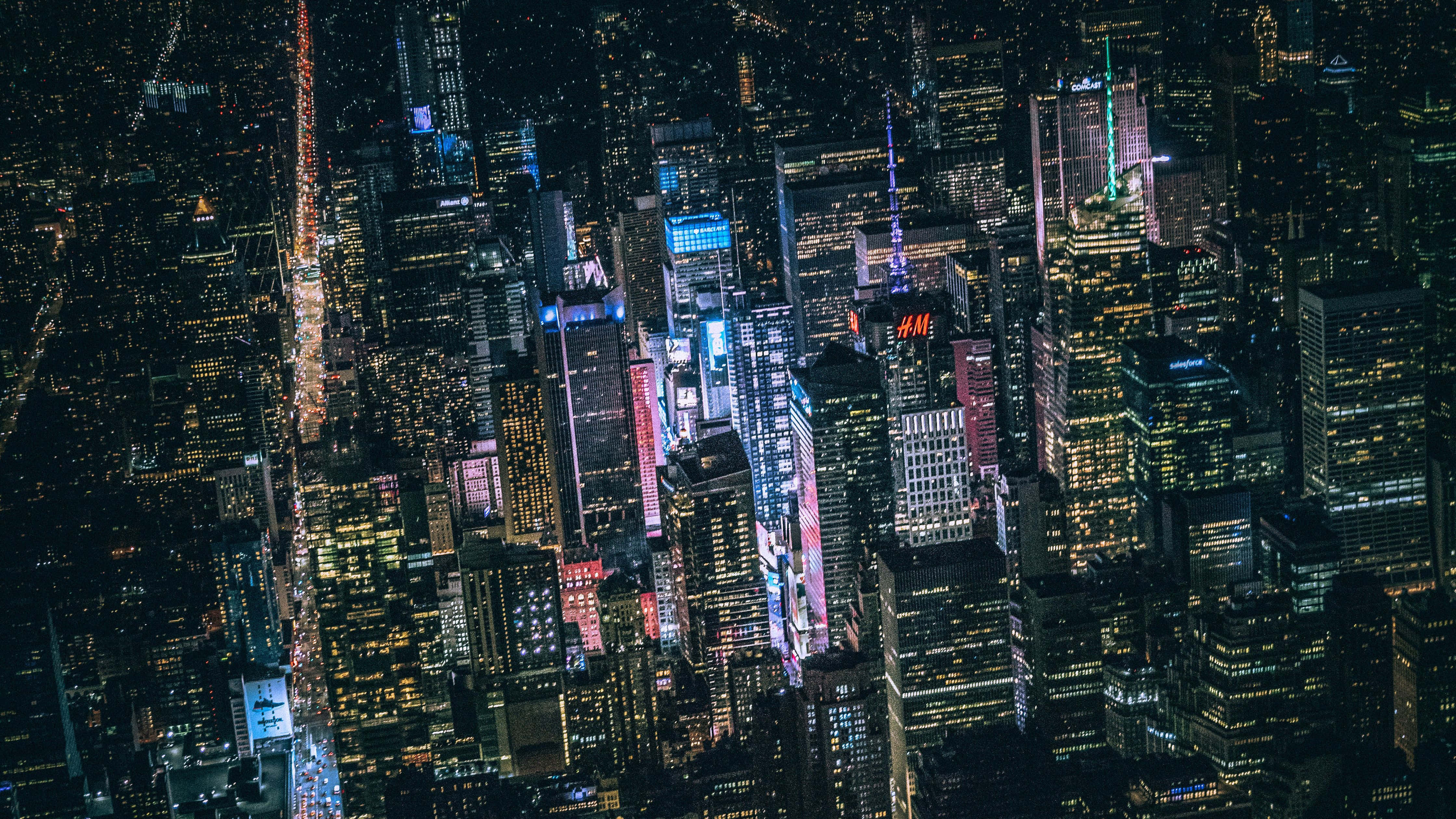 暗夜城市 桌布 壁紙 — 夜晚密集城市景觀的鳥瞰圖，高聳的摩天大樓閃爍著色彩繽紛的霓虹燈，下方是繁華的街道。