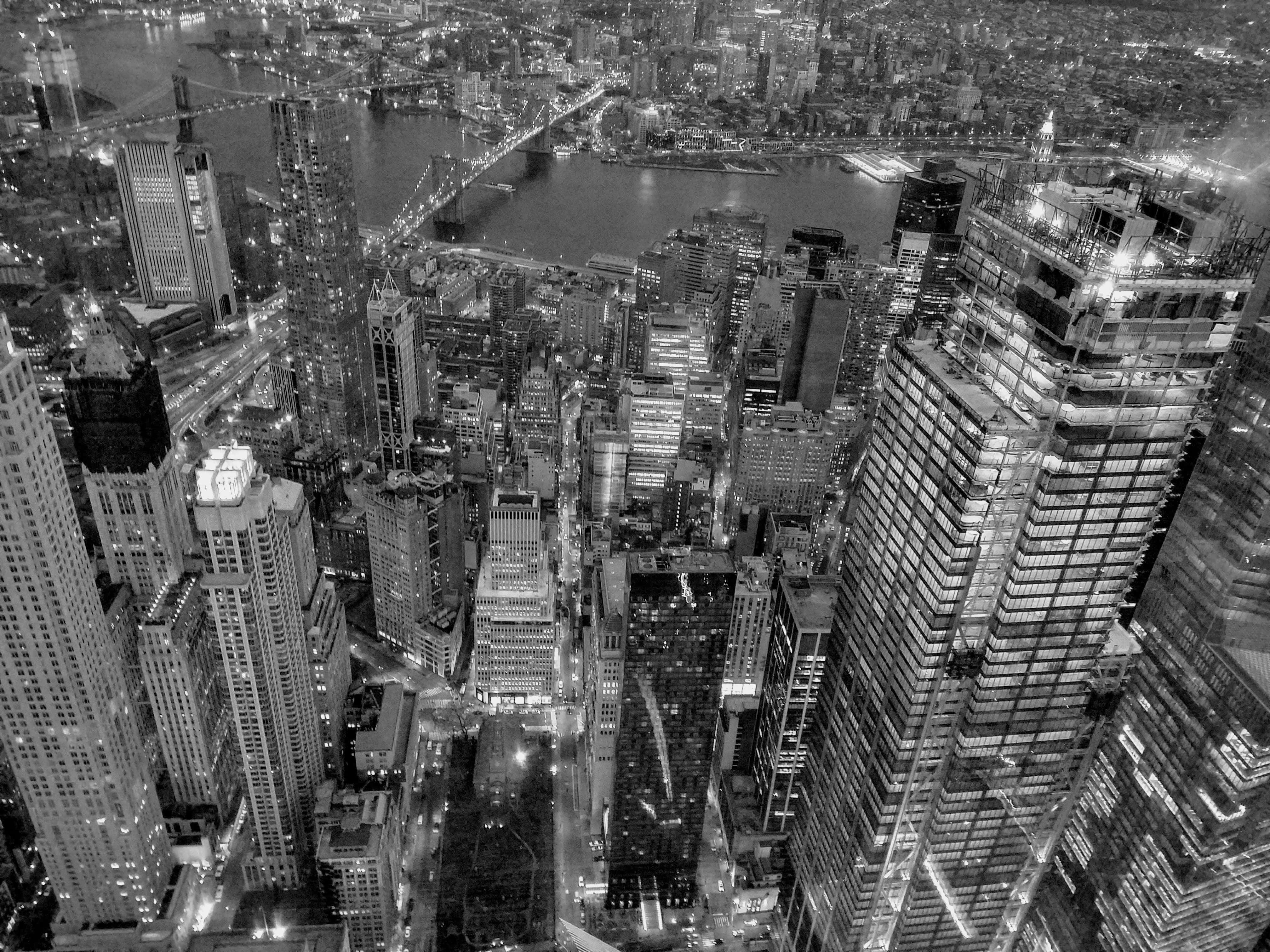 Black And White Cityscape 桌布 壁紙 — 夜晚密集城市景觀的黑白航拍圖，帶有發光的摩天大樓和水面上的橋樑。
